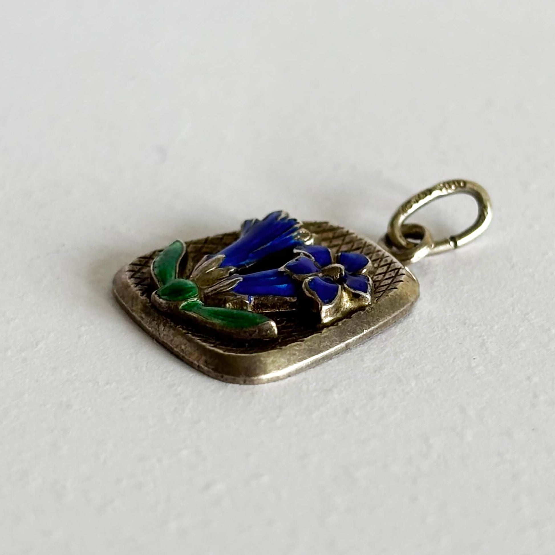 Silver pendant with blue and green floral design on a white background