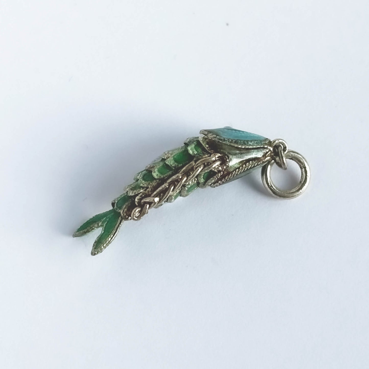 Vintage silver green enamel wiggly fish charm on a white background.