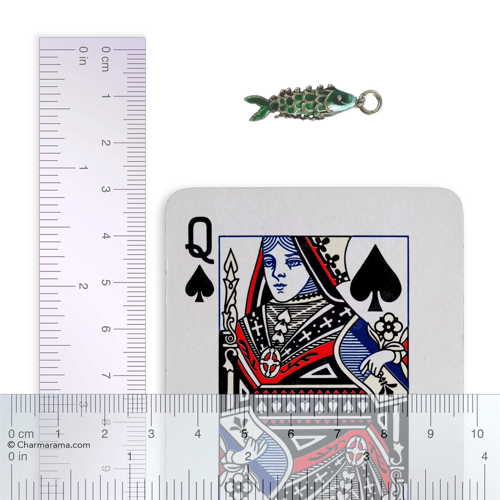 Vintage silver green enamel articulated fish charm with playing card and ruler for scale on a white background.