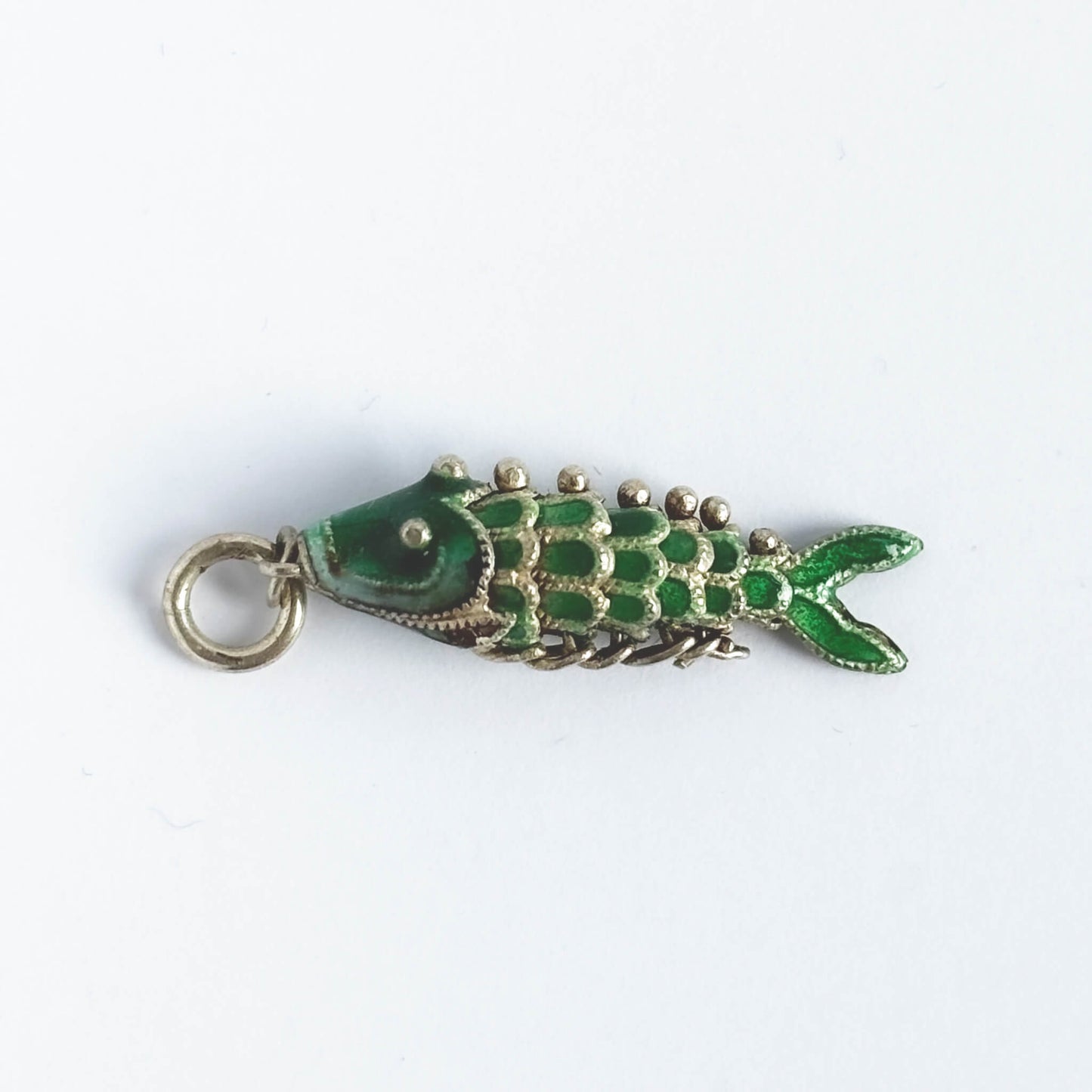 Vintage silver green enamel articulated fish charm on a white background.