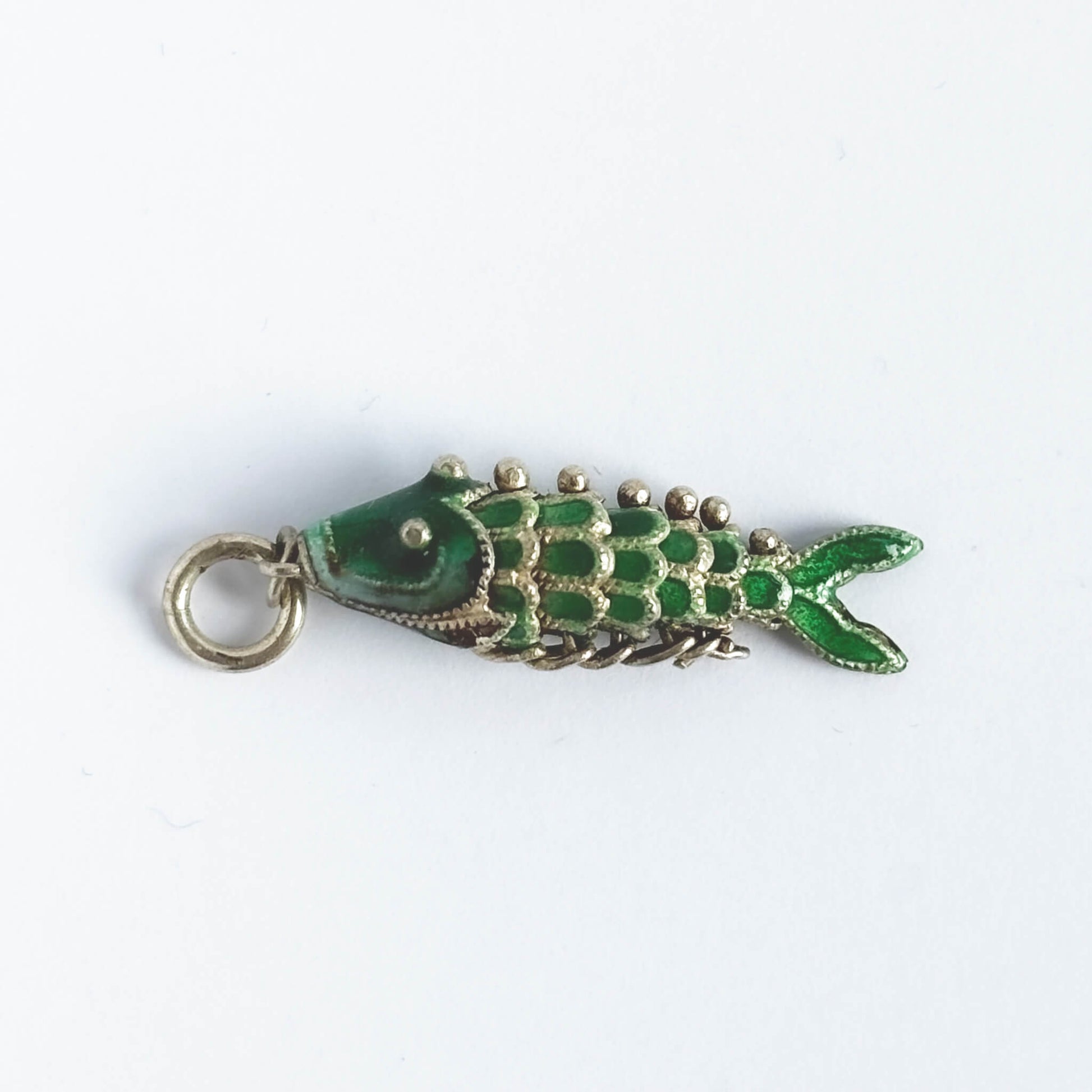 Vintage silver green enamel articulated fish charm on a white background.