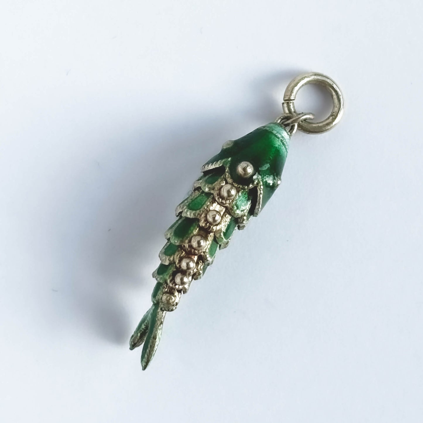 Vintage silver green enamel articulated fish charm on a white background.