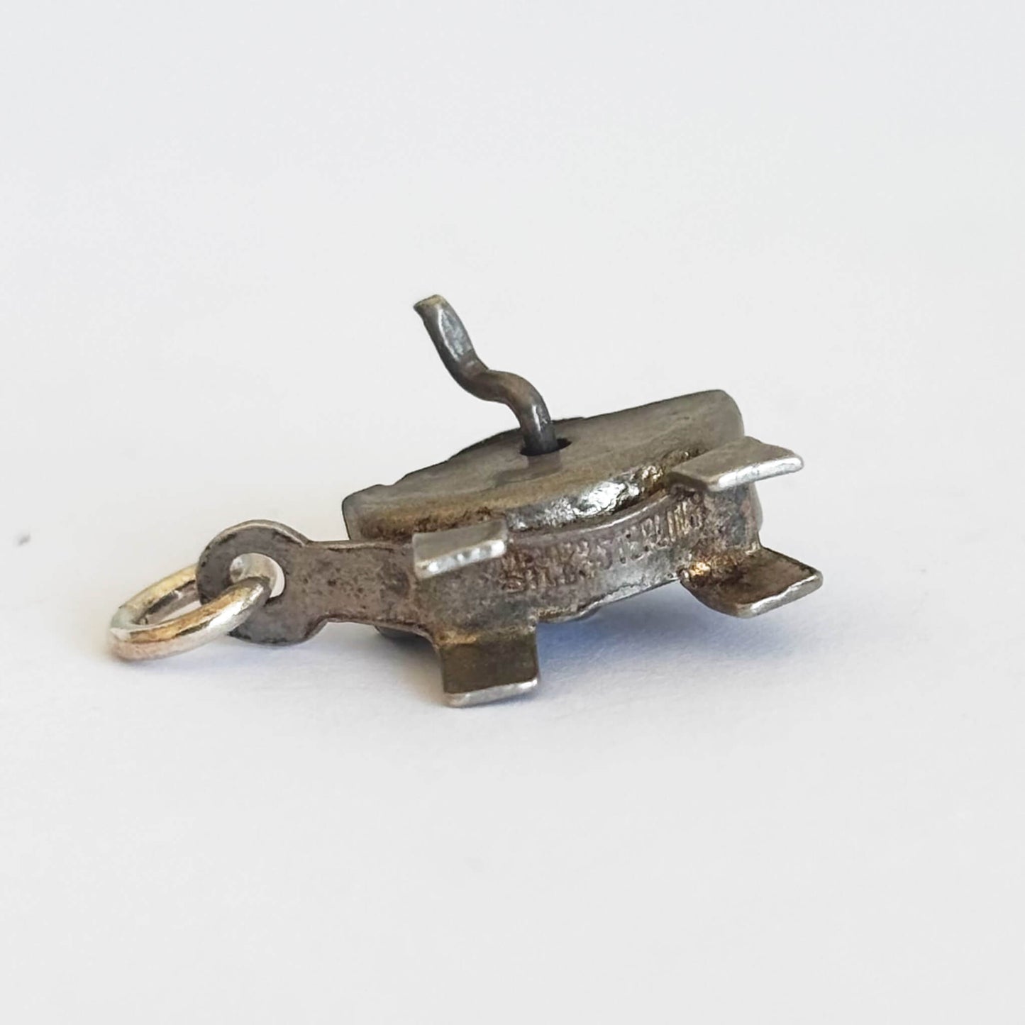 underside of vintage silver grindstone charm on a white background
