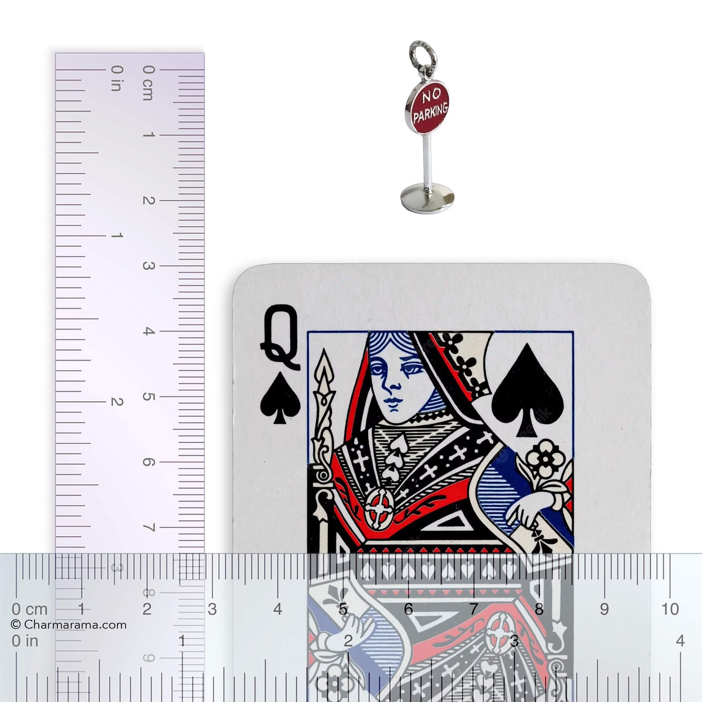 A vintage sterling silver no parking sign charm with ruler and playing card for scale on a white background.