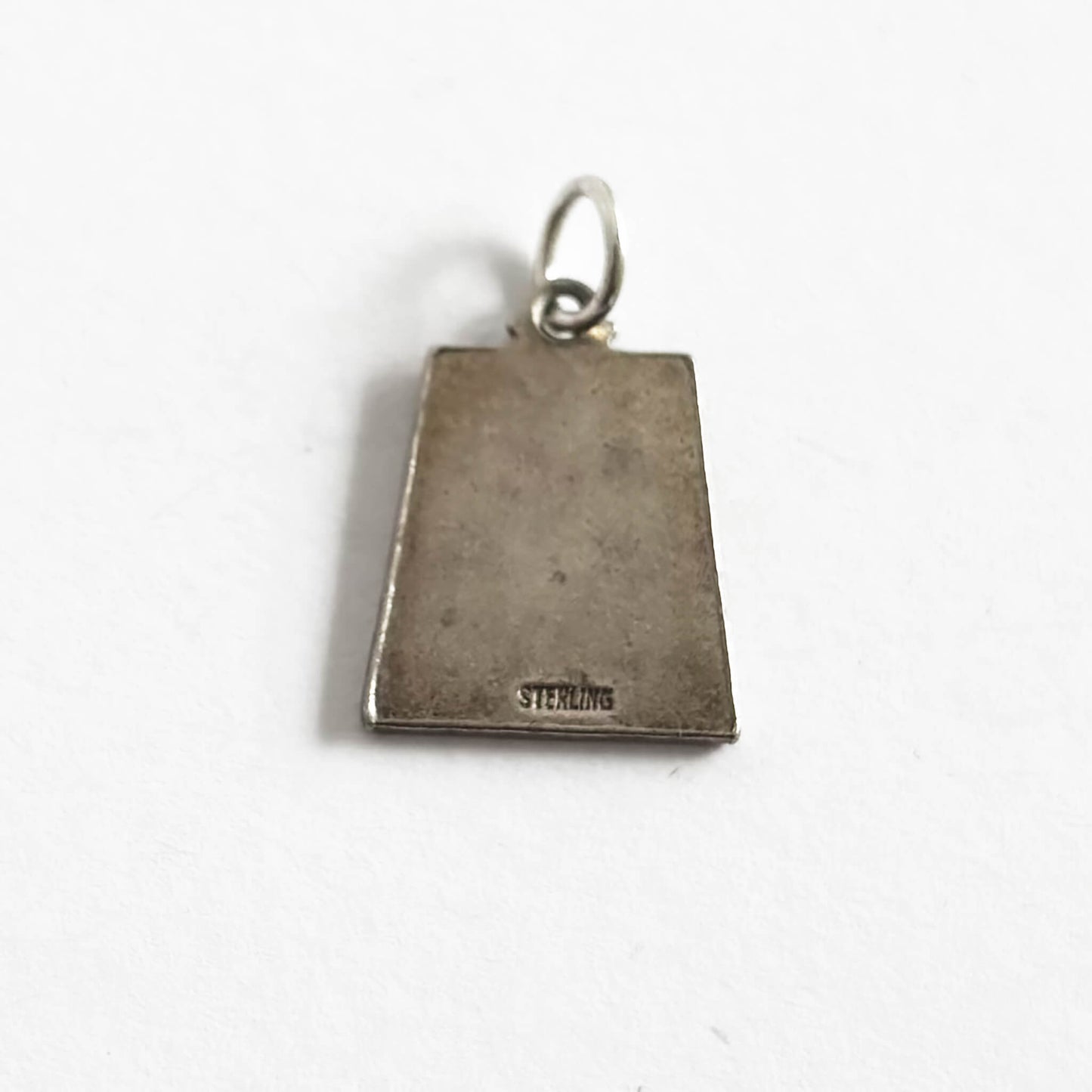 Back of silver trapezoid shape pendant with Libra zodiac sign and 'September' text with four dark blue enamel corner squares, on a white background
