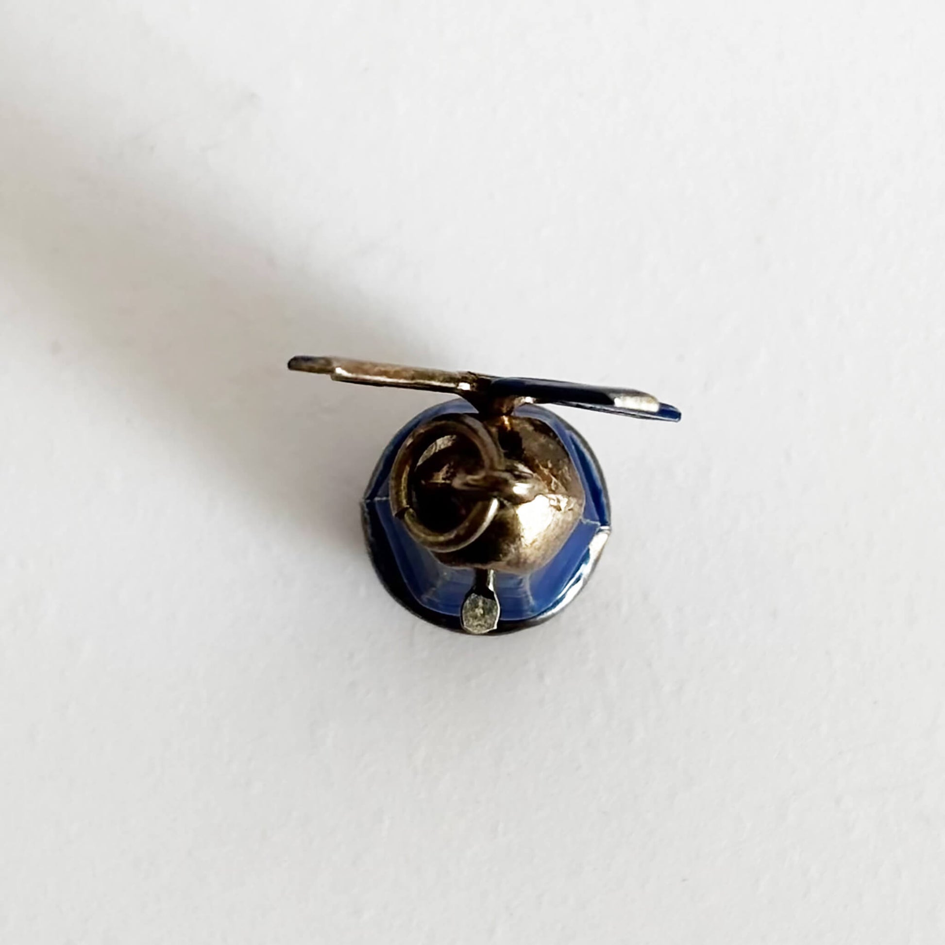 Vintage silver and blue enamel windmill charm viewed from top on a white background