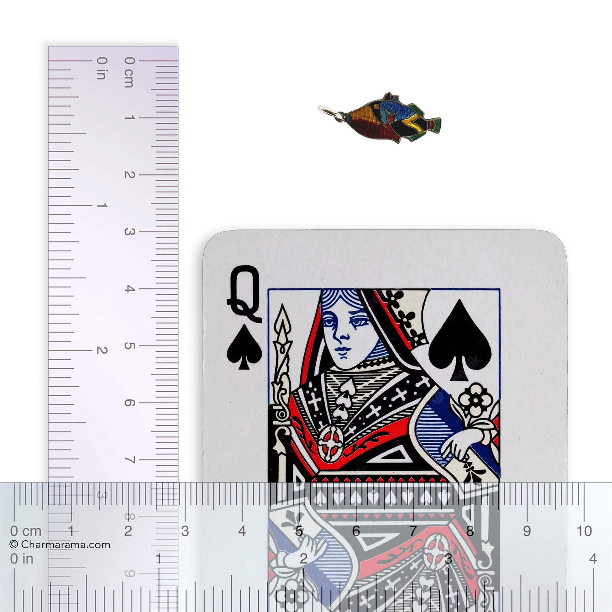 Vintage silver and colourful enamel tropical fish charm with playing card and ruler for scale on a white background