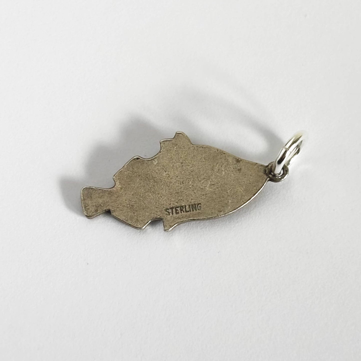 Back of a vintage silver tropical fish charm on a white background