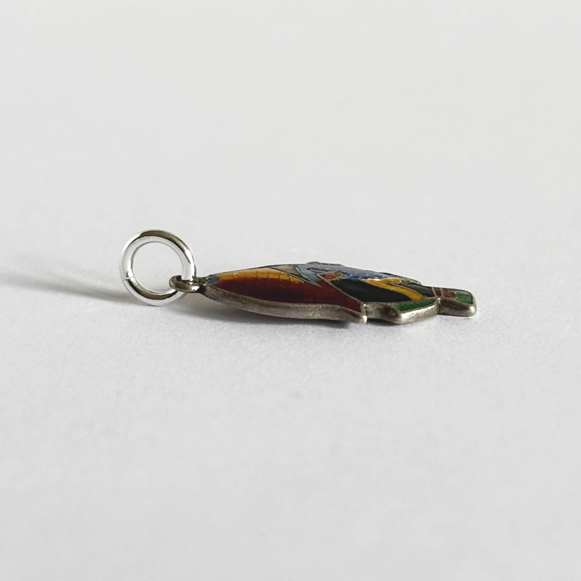 Side view of a vintage silver and colourful enamel tropical fish charm on a white background