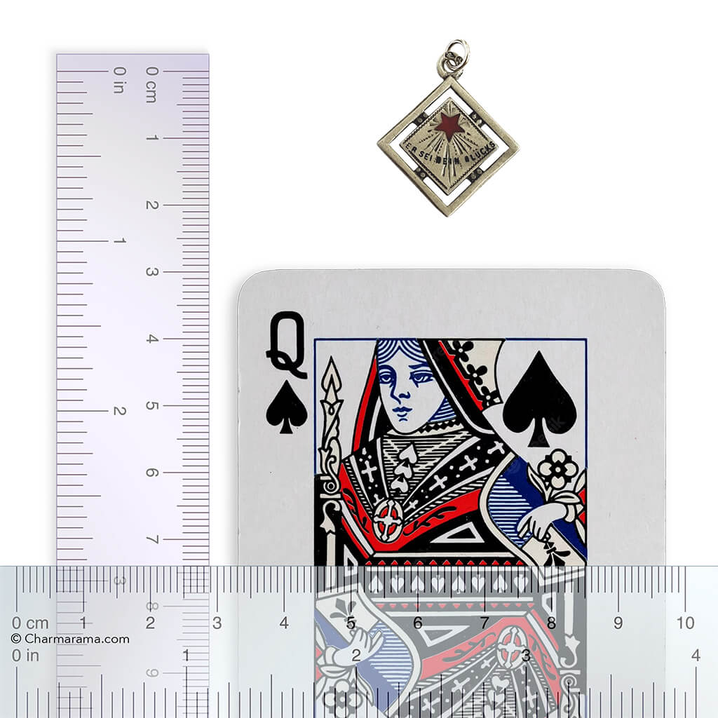 An antique silver and enamel Austrian lucky star charm on a white background with playing card and ruler for scale