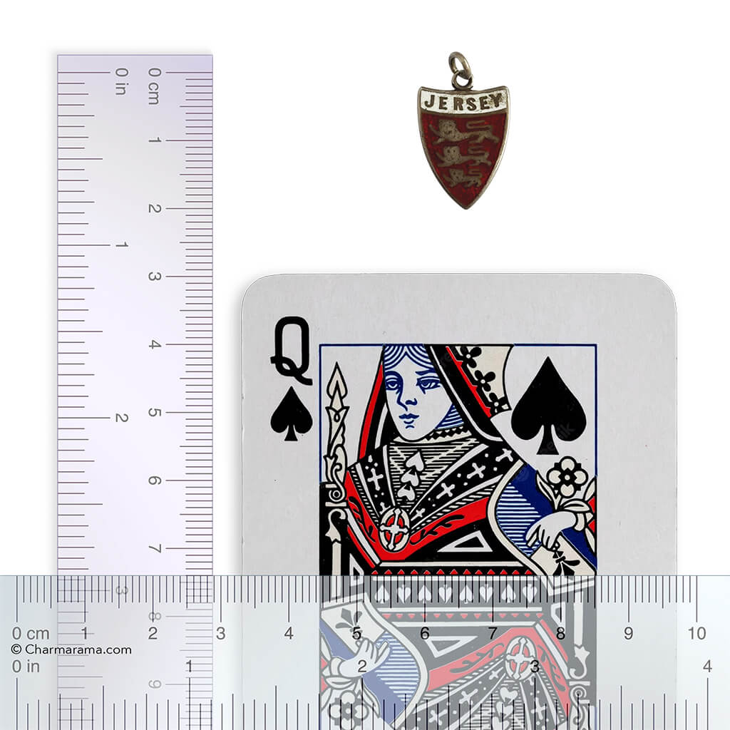 Antique Jersey travel shield charm with ruler and playing card for scale, on white background.