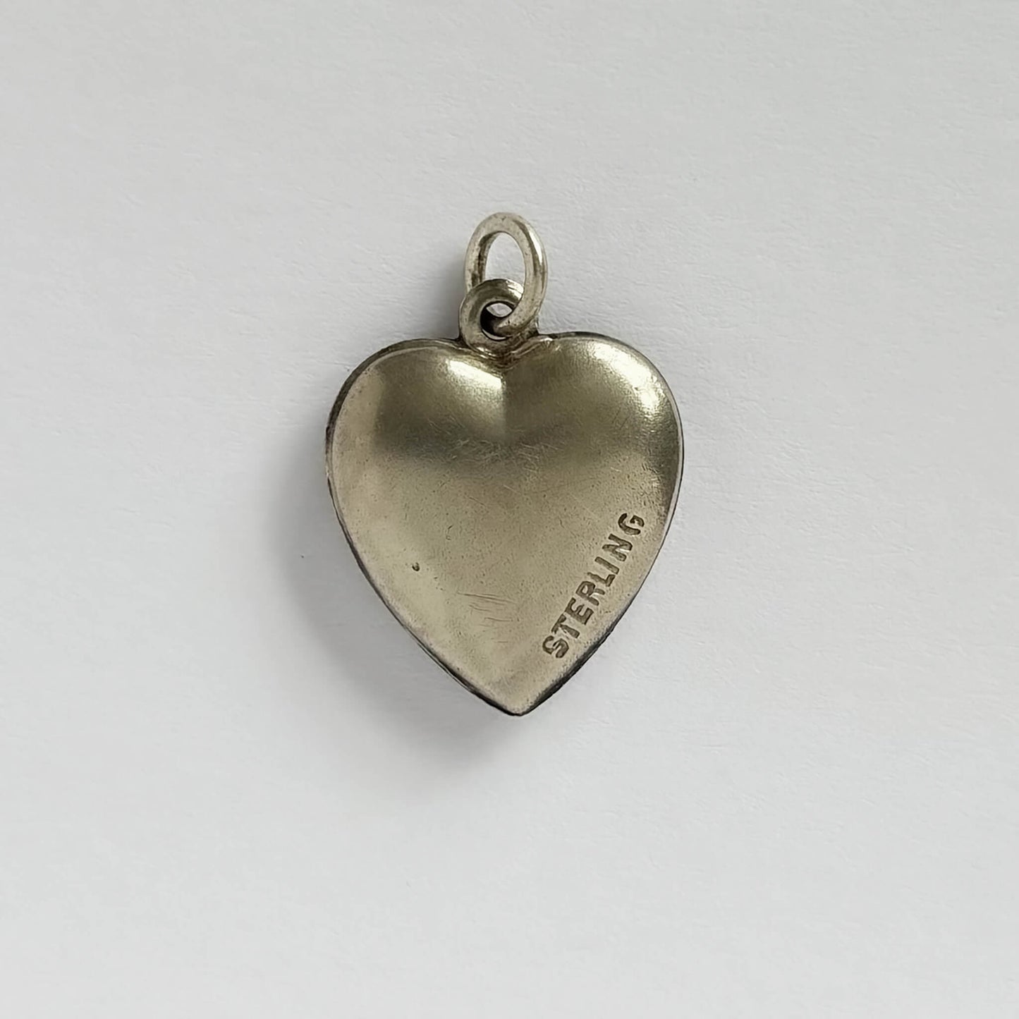 A vintage sterling silver heart charm with white guilloche enamel behind a pink rose