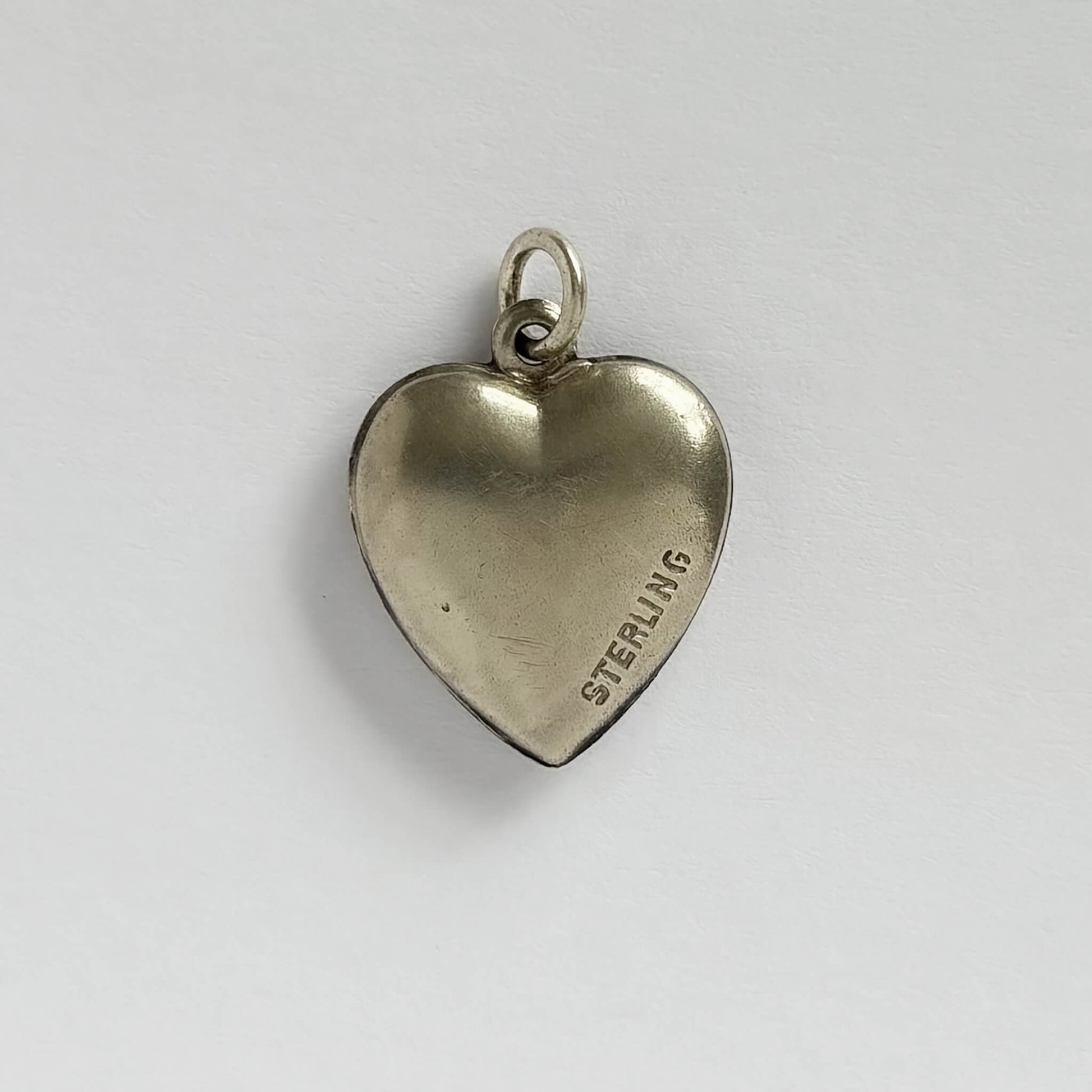 A vintage sterling silver heart charm with white guilloche enamel behind a pink rose