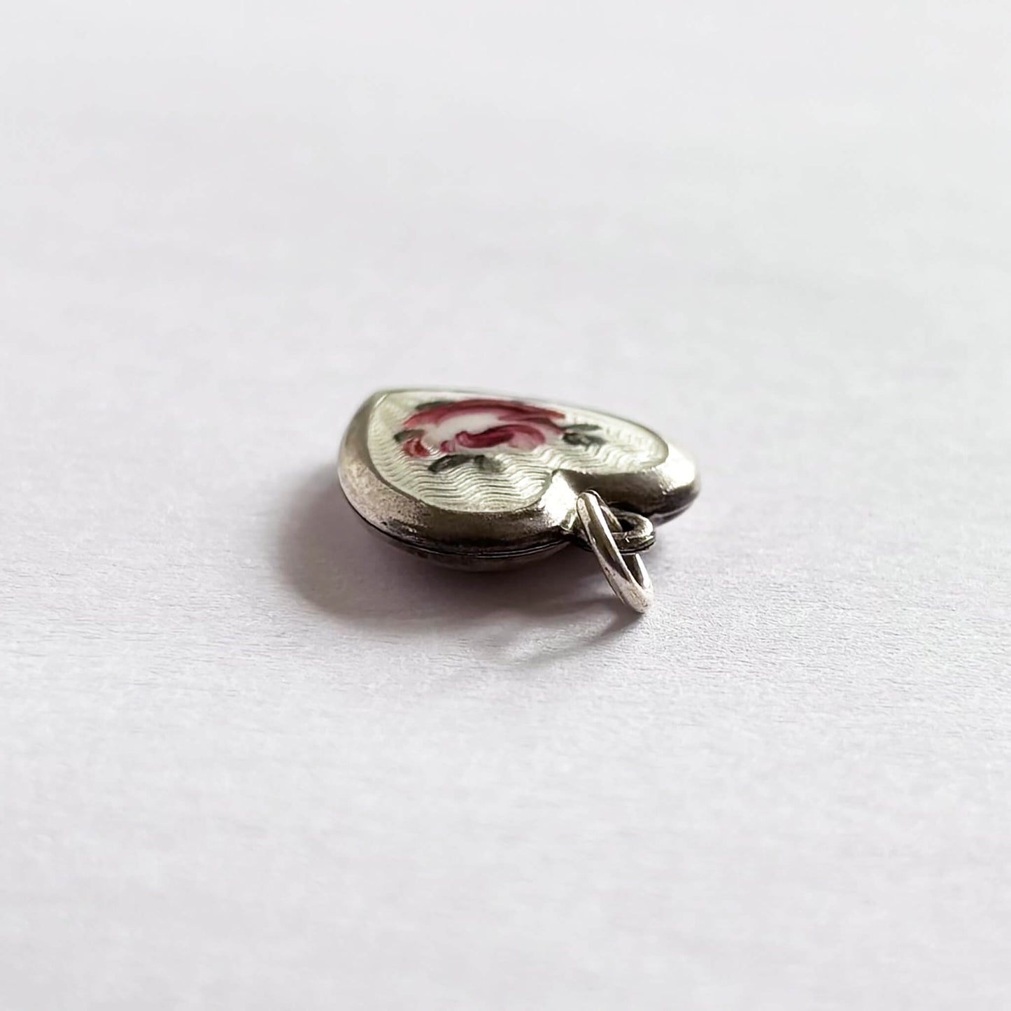 Top view of a vintage heart charm with pink rose on white background in sterling silver and guilloche enamel