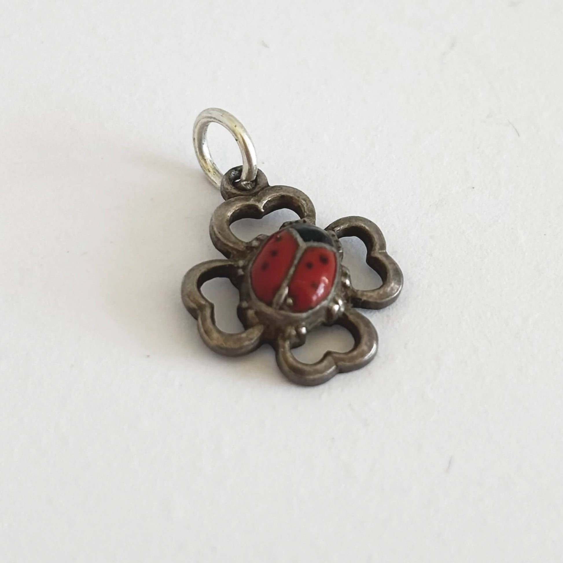 Silver pendant with a red ladybug design on a white background