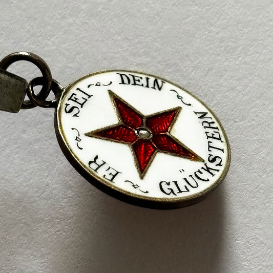charm with red star and German text on a light gray background