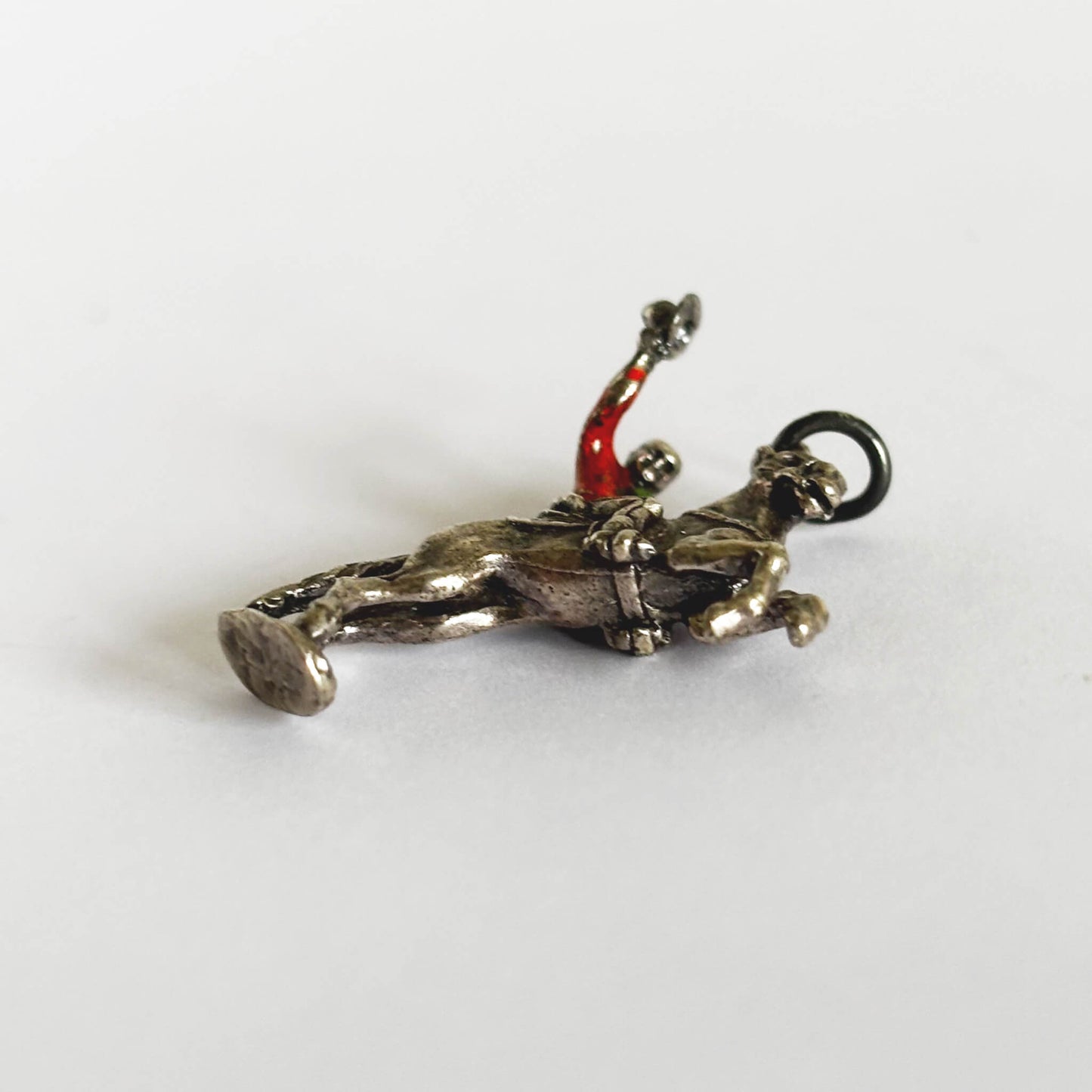 Cowboy on rearing horse silver charm with red enamel shirt on light grey background