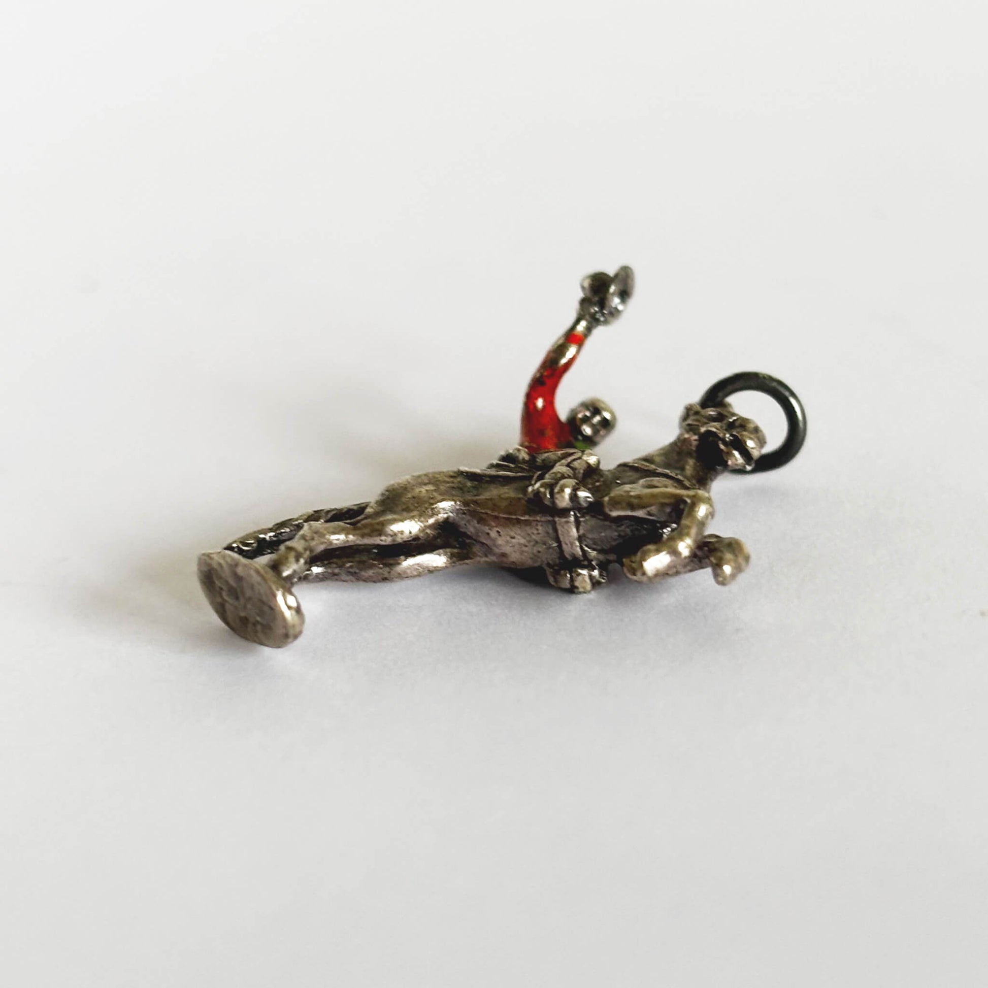 Cowboy on rearing horse silver charm with red enamel shirt on light grey background