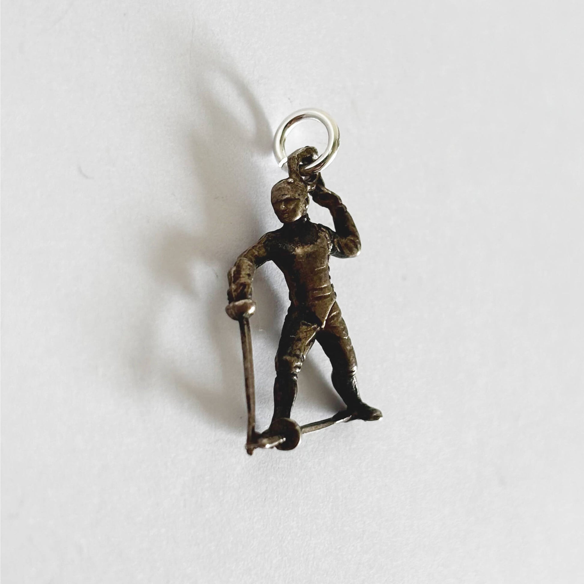 Vintage silver charm of a fencer holding a sword on a white background