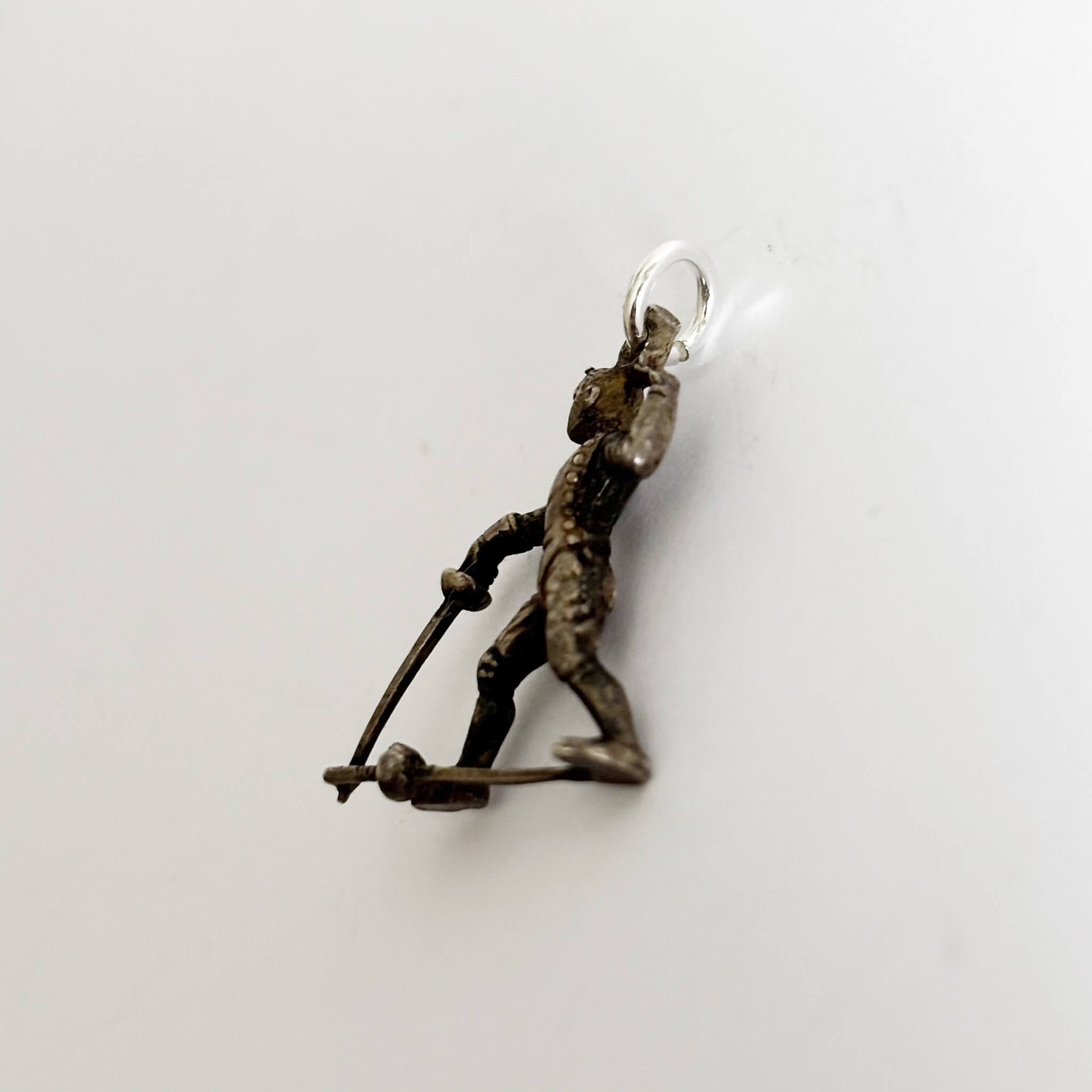 Vintage silver charm of a fencer holding a sword on a white background