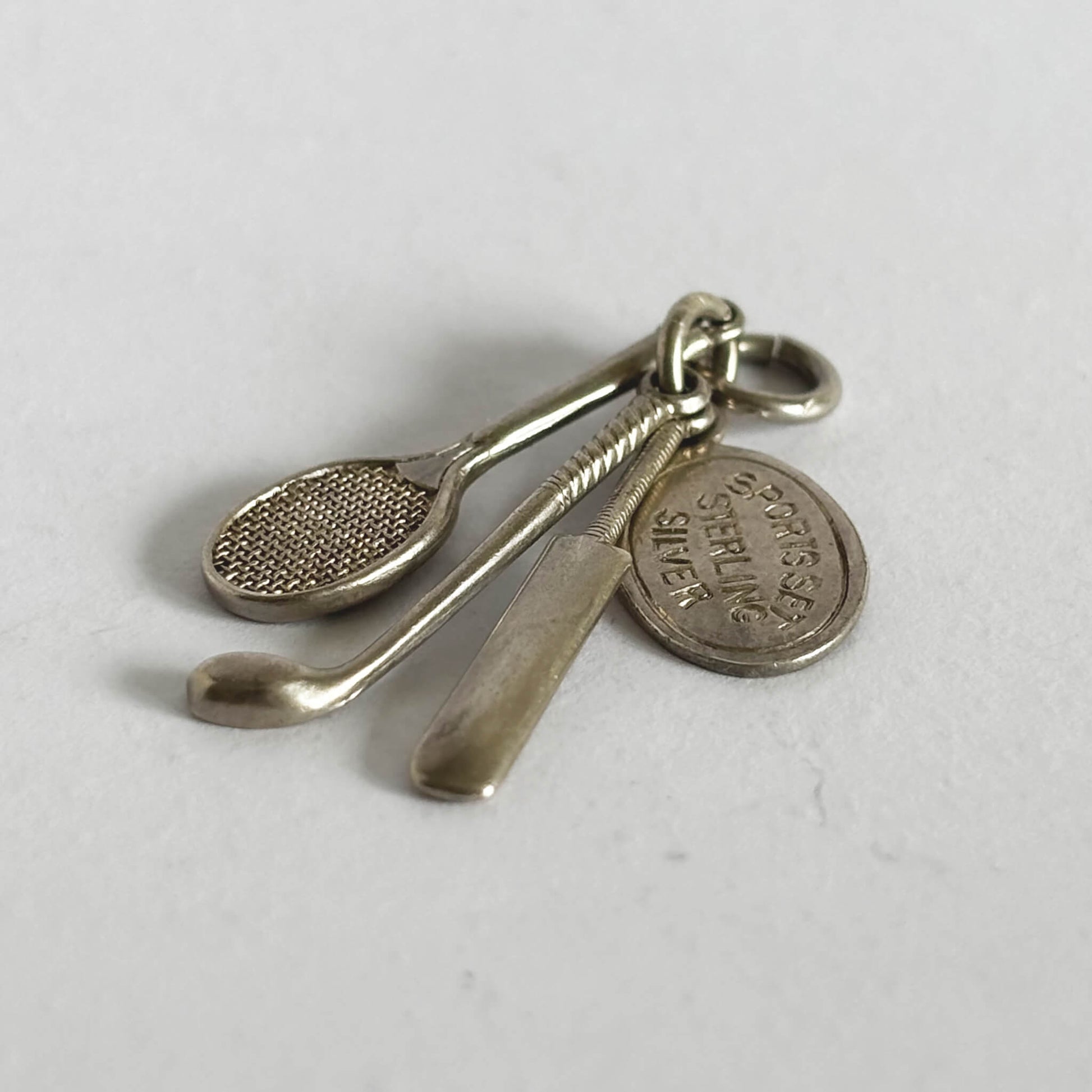 silver charm comprising a tennis racquet, golf club, cricket bat on a light grey background