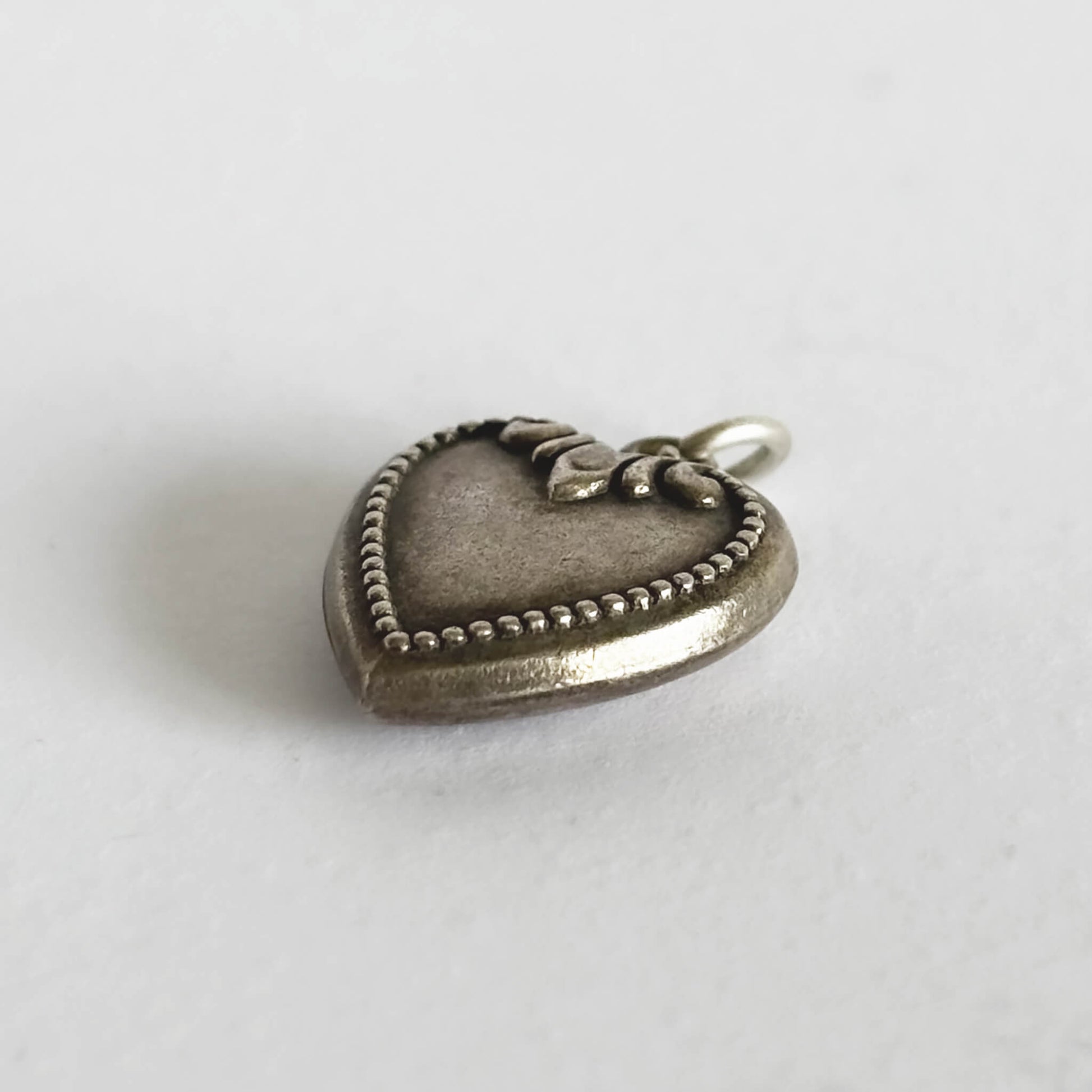 Side view of a sterling silver antique heart charm on a white background