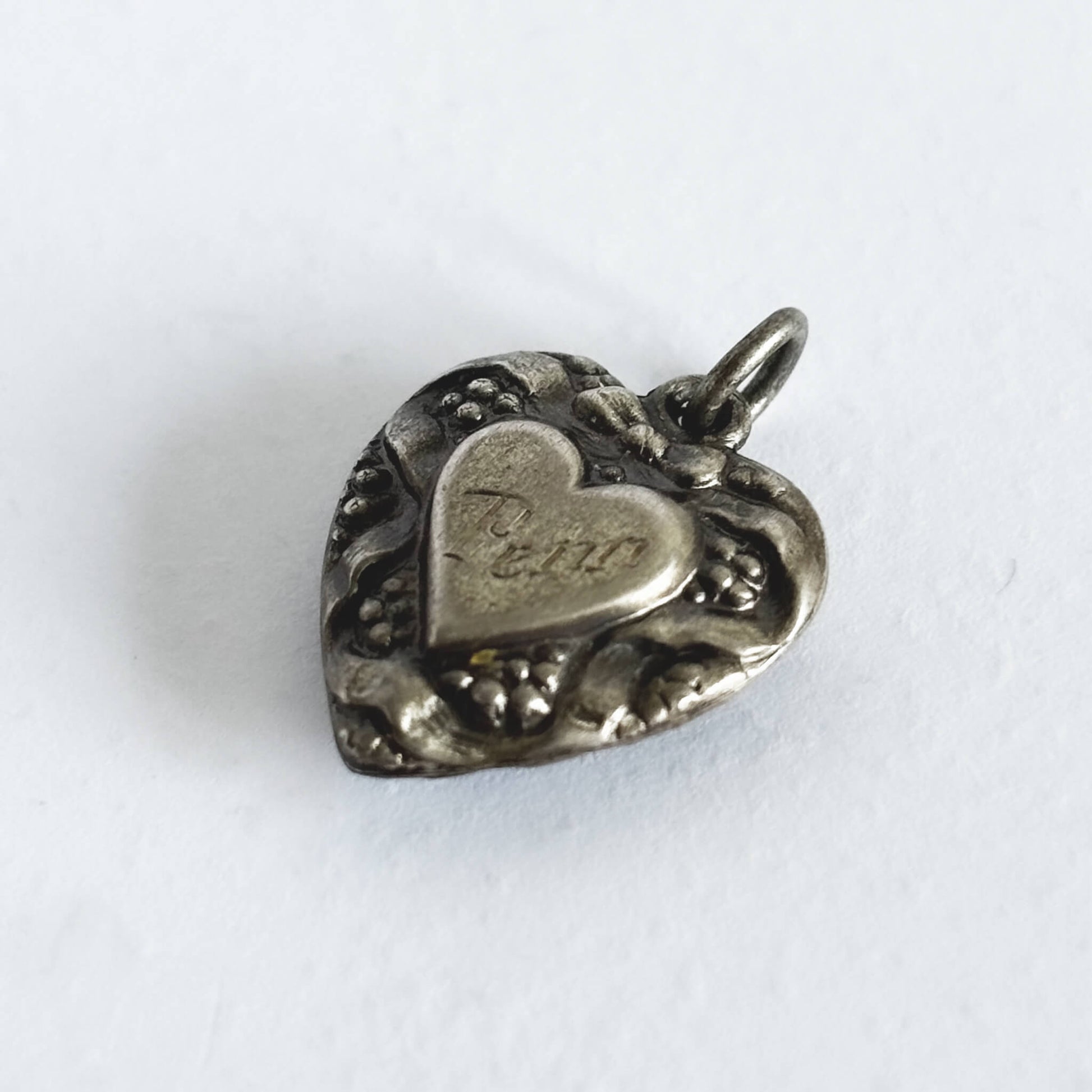 Silver heart-shaped pendant with engraved text on a white background