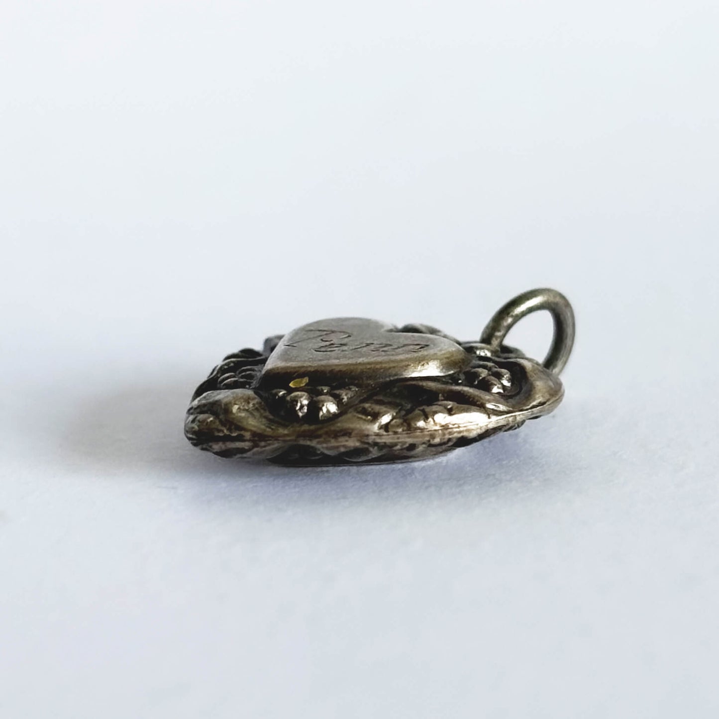 Side view of decorative antique silver heart charm on white background