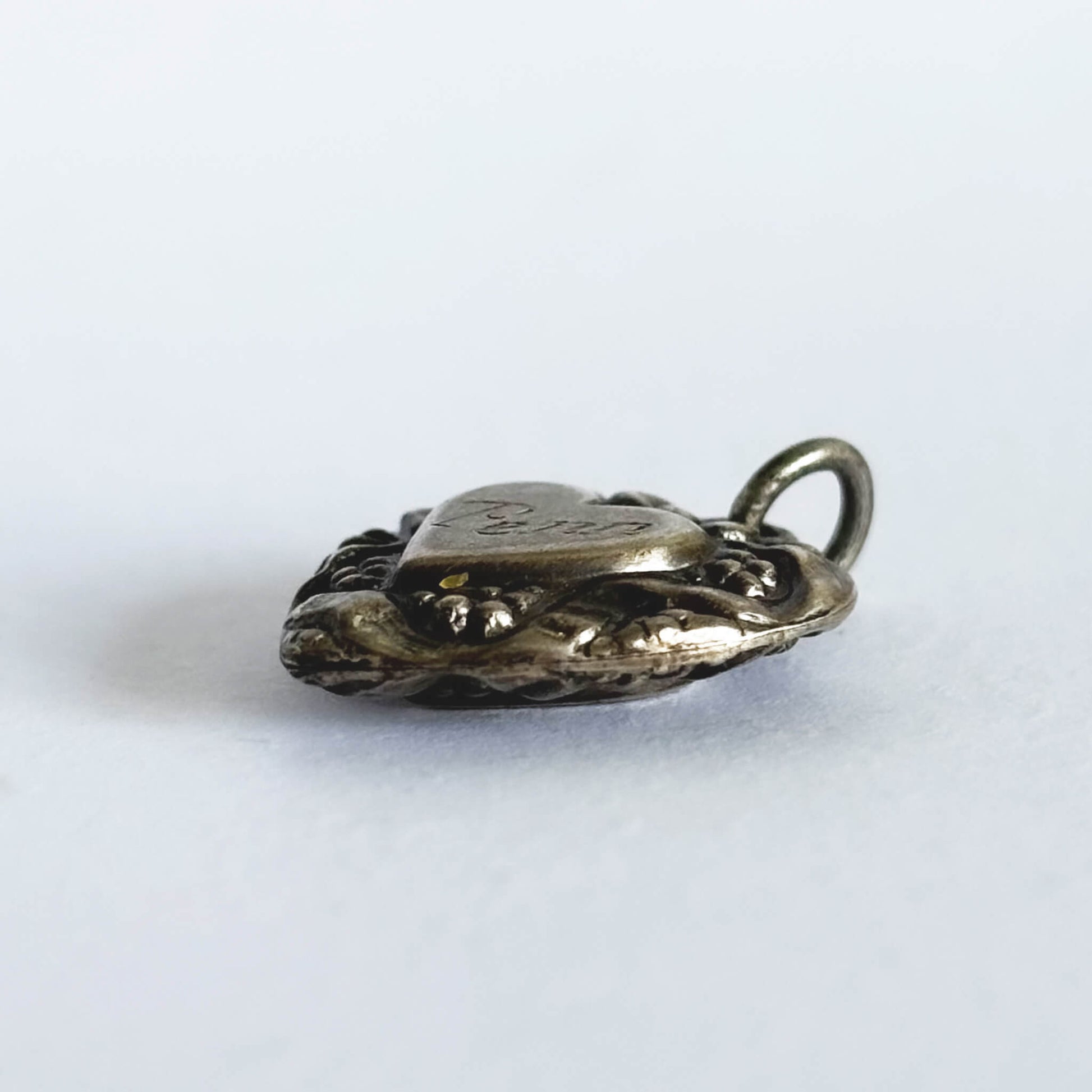 Side view of decorative antique silver heart charm on white background