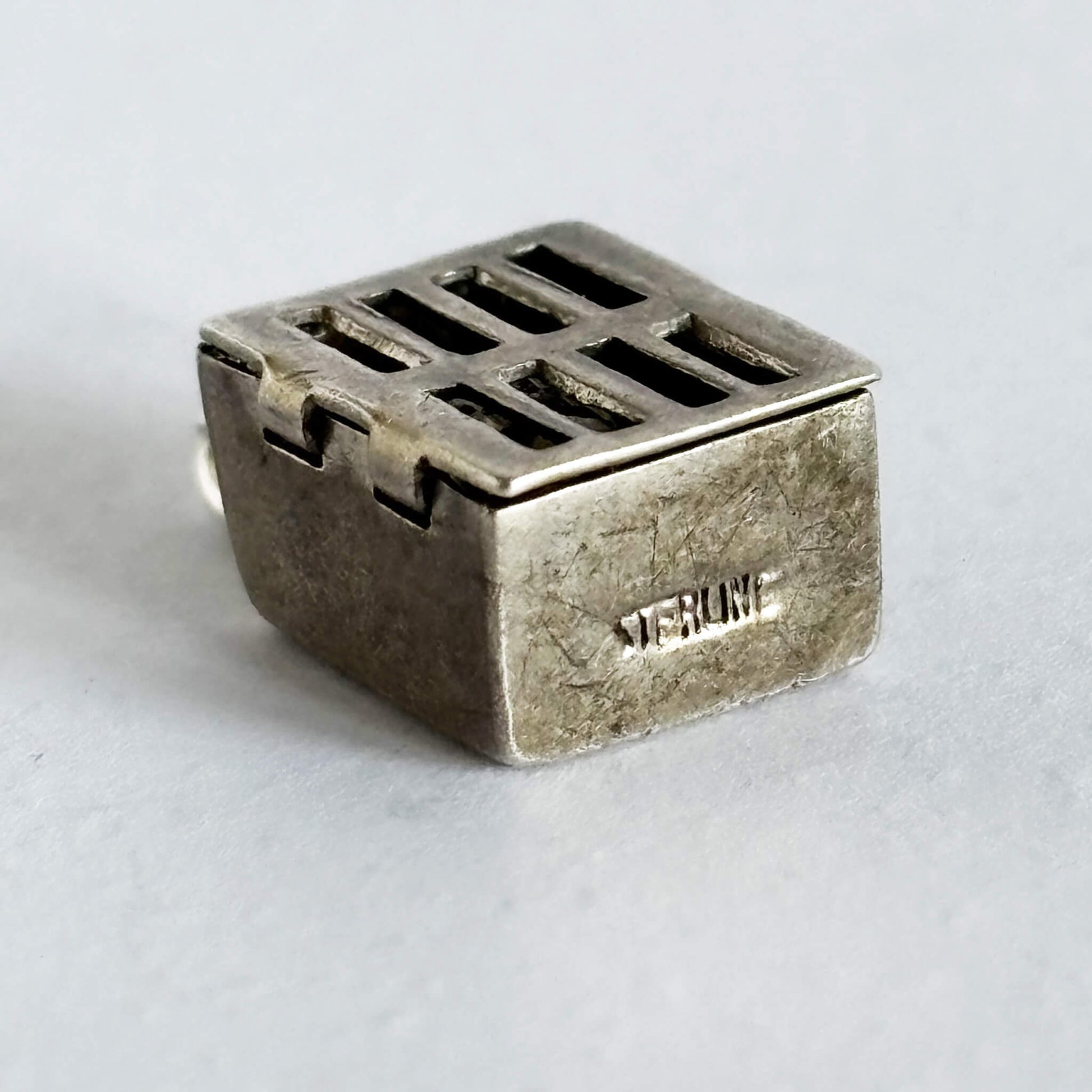 Sterling silver prison cell charm on a light grey background
