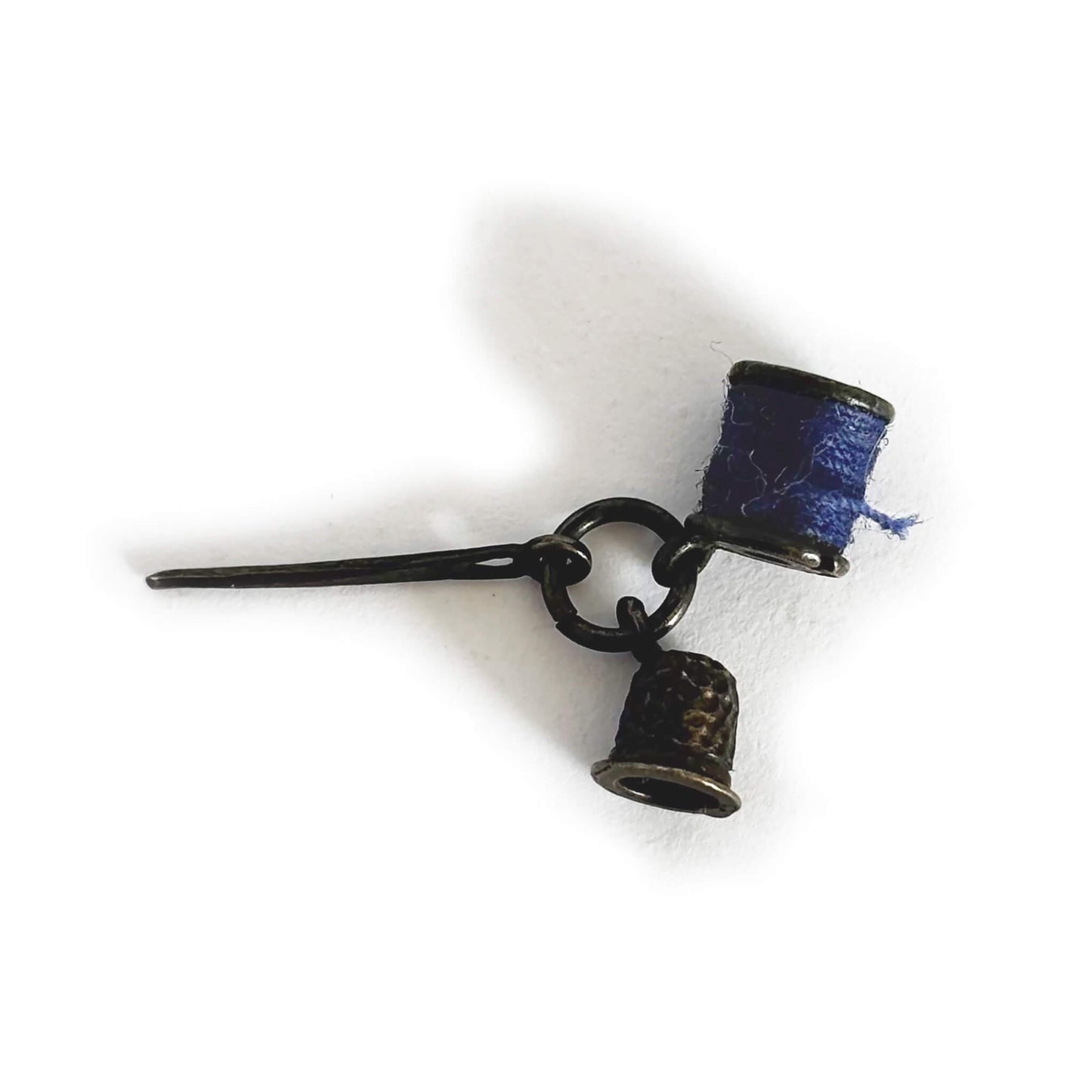 Sterling silver thimble needle and cotton reel charm on a white background