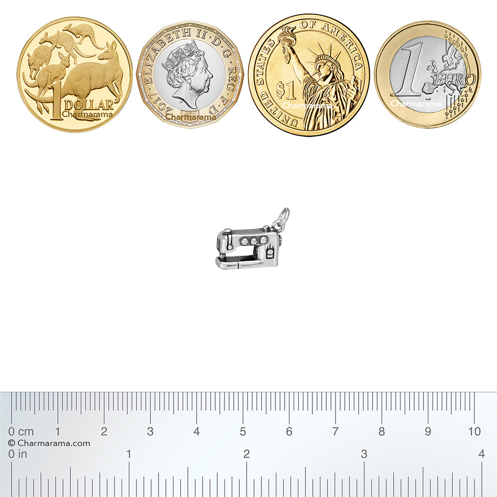 Silver sewing machine charm with a set of coins from different countries and a ruler for scale on a white background.
