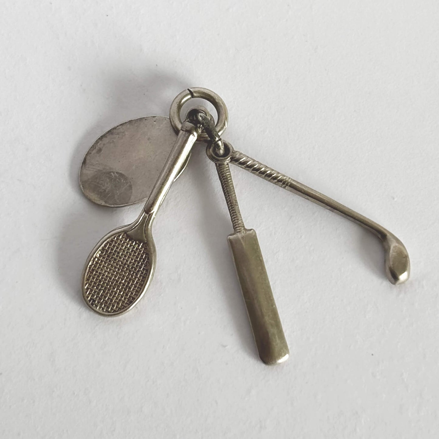 silver charm comprising a tennis racquet, golf club, cricket bat on a grey background