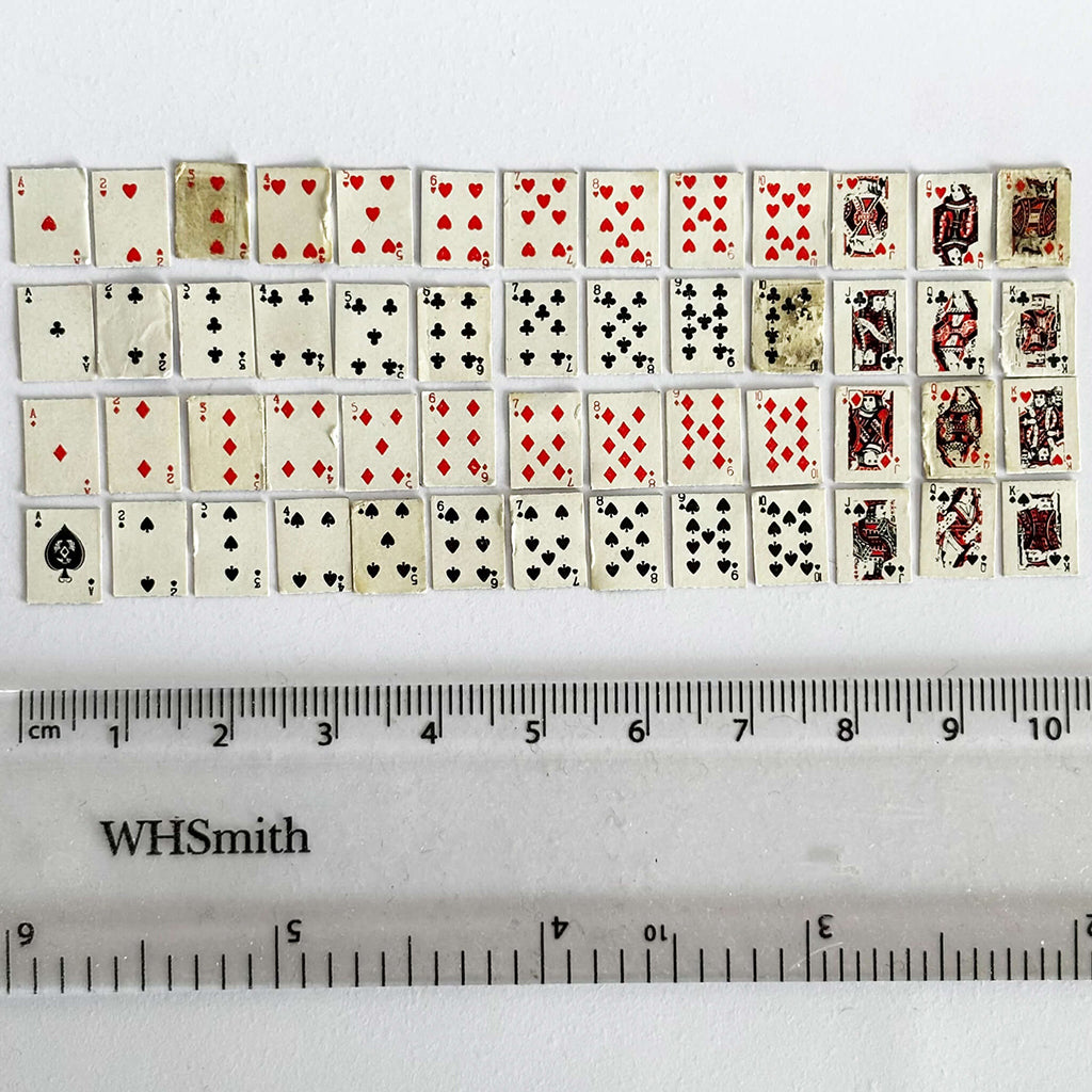 Set of miniature playing cards with a ruler for scale on a white background