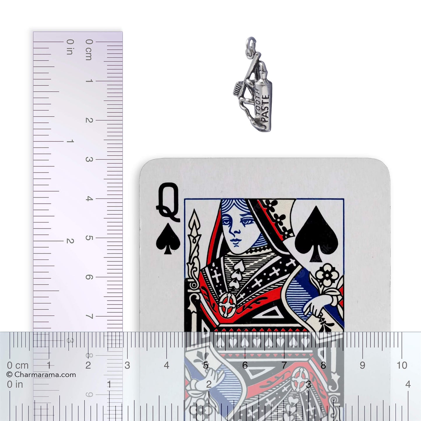 Silver toothpaste and toothbrush charm with playing card and ruler for scale on white background