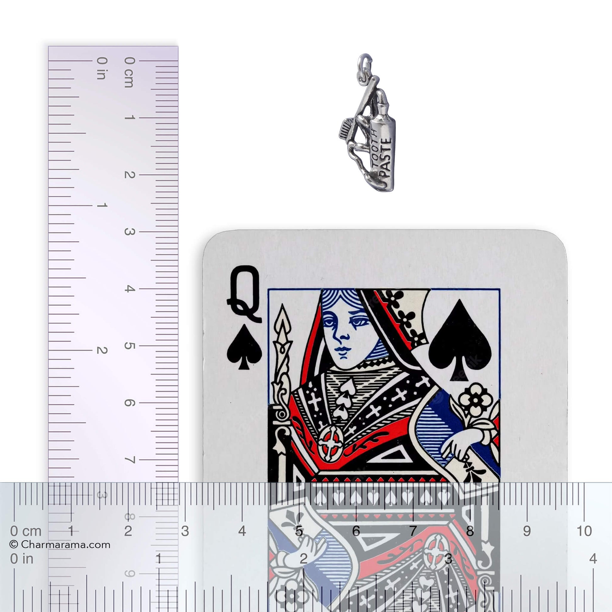 Silver toothpaste and toothbrush charm with playing card and ruler for scale on white background