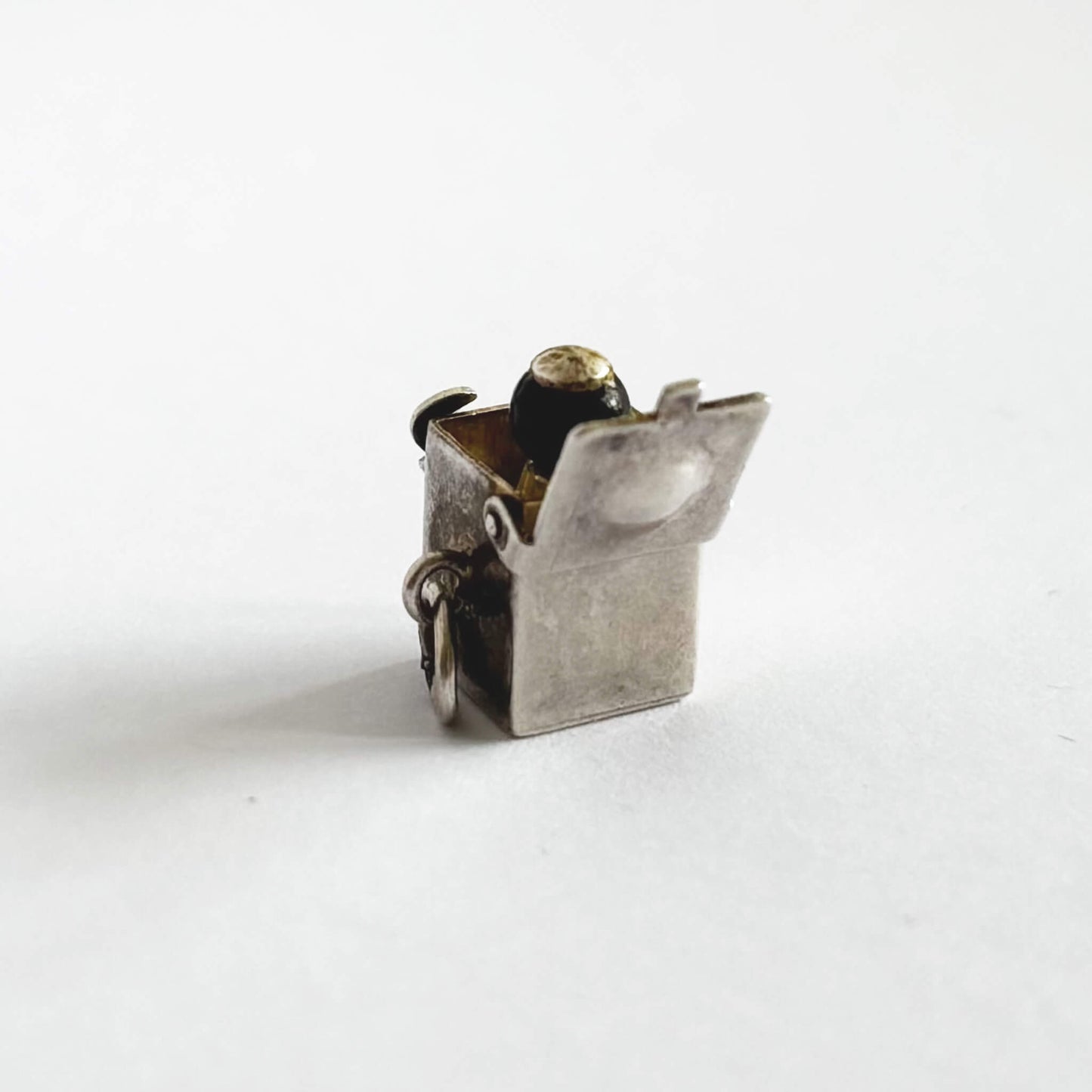 Back of vintage sterling silver Jack-in-the-box charm, open to reveal tiny figure, on white background