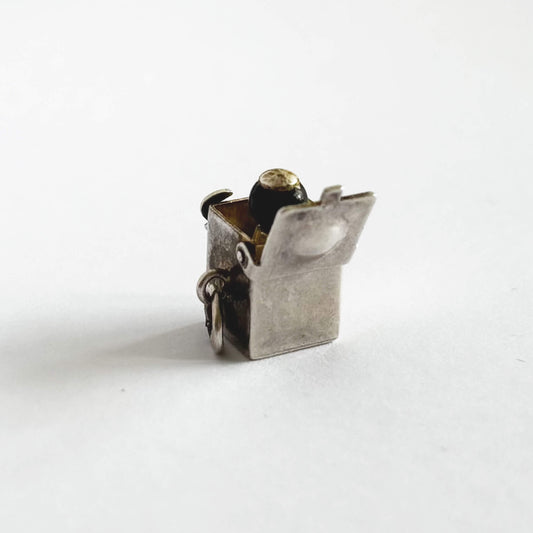 Back of vintage sterling silver Jack-in-the-box charm, open to reveal tiny figure, on white background