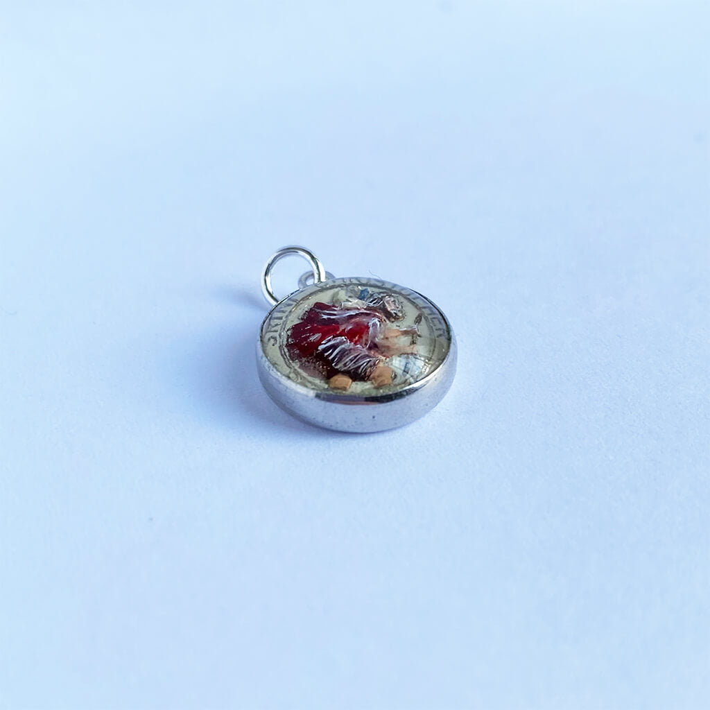 Round silver pendant with Saint Christopher under a glass dome on a light blue background
