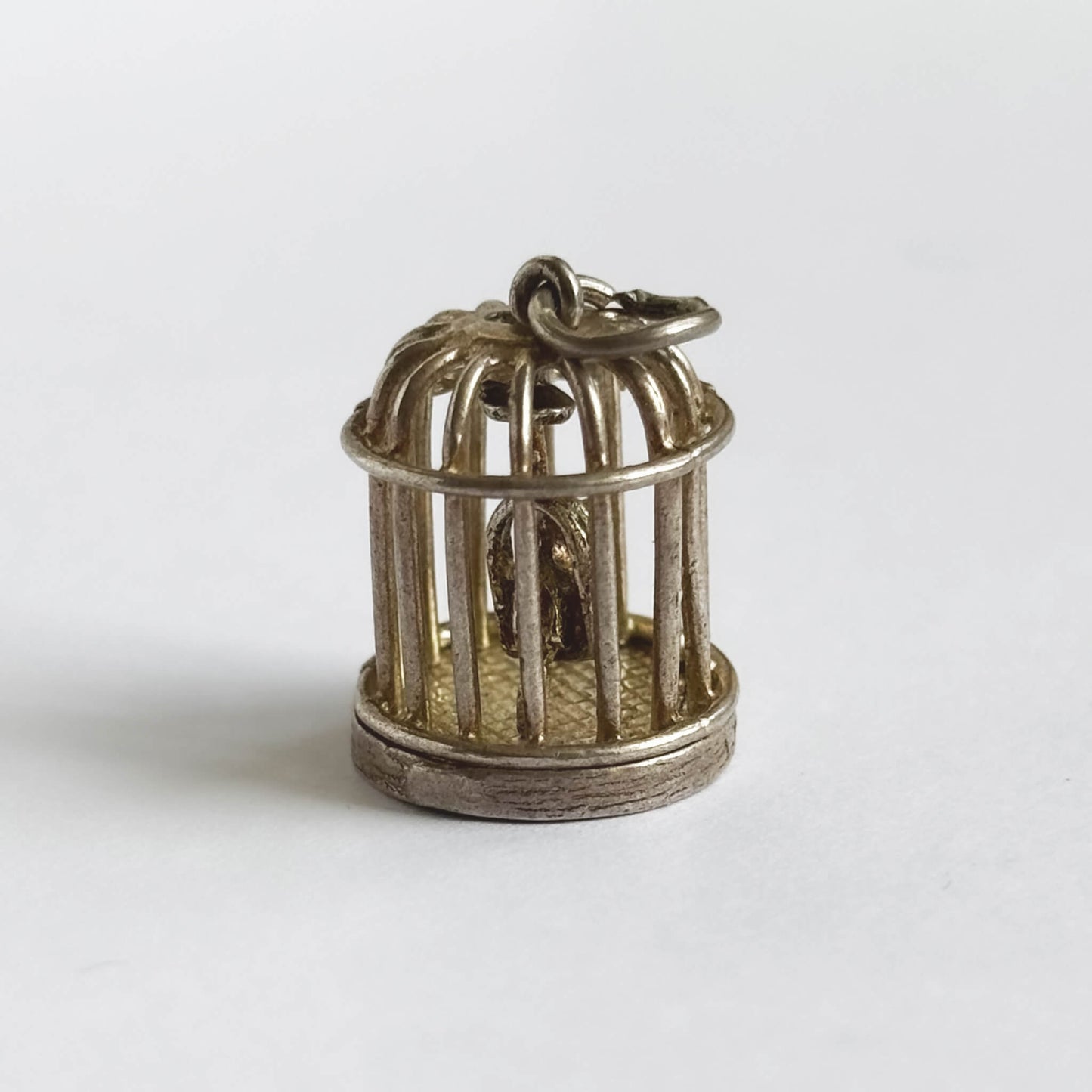 Vintage silver bird in a cage charm on a white background.
