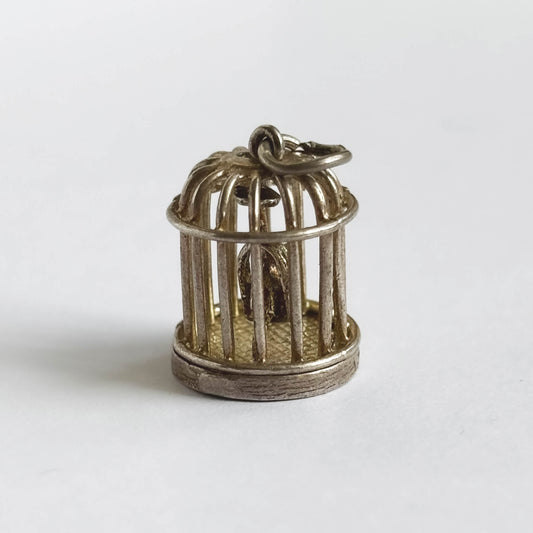 Vintage silver bird in a cage charm on a white background.