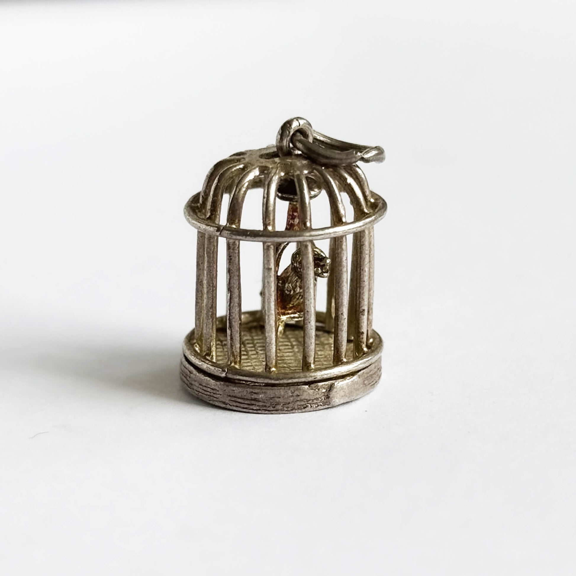 Vintage silver bird in a cage charm on a pale grey background.