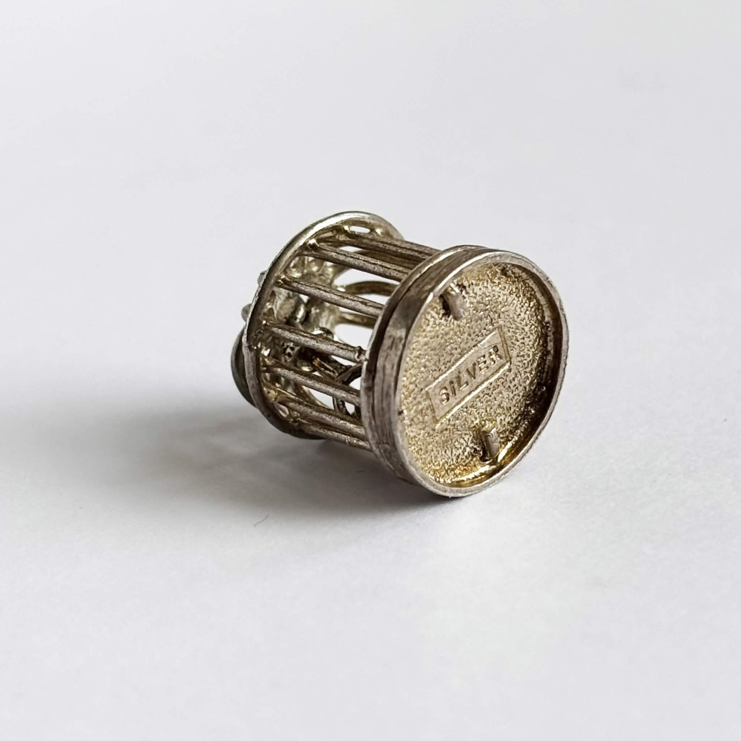 Vintage silver bird in a cage charm on a white background.