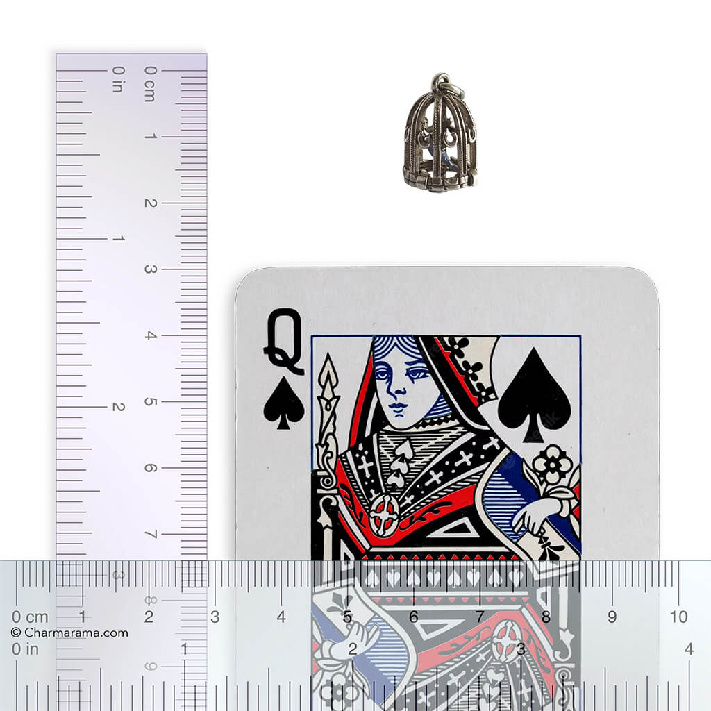 Small silver bird cage charm next to a playing card with a ruler for scale