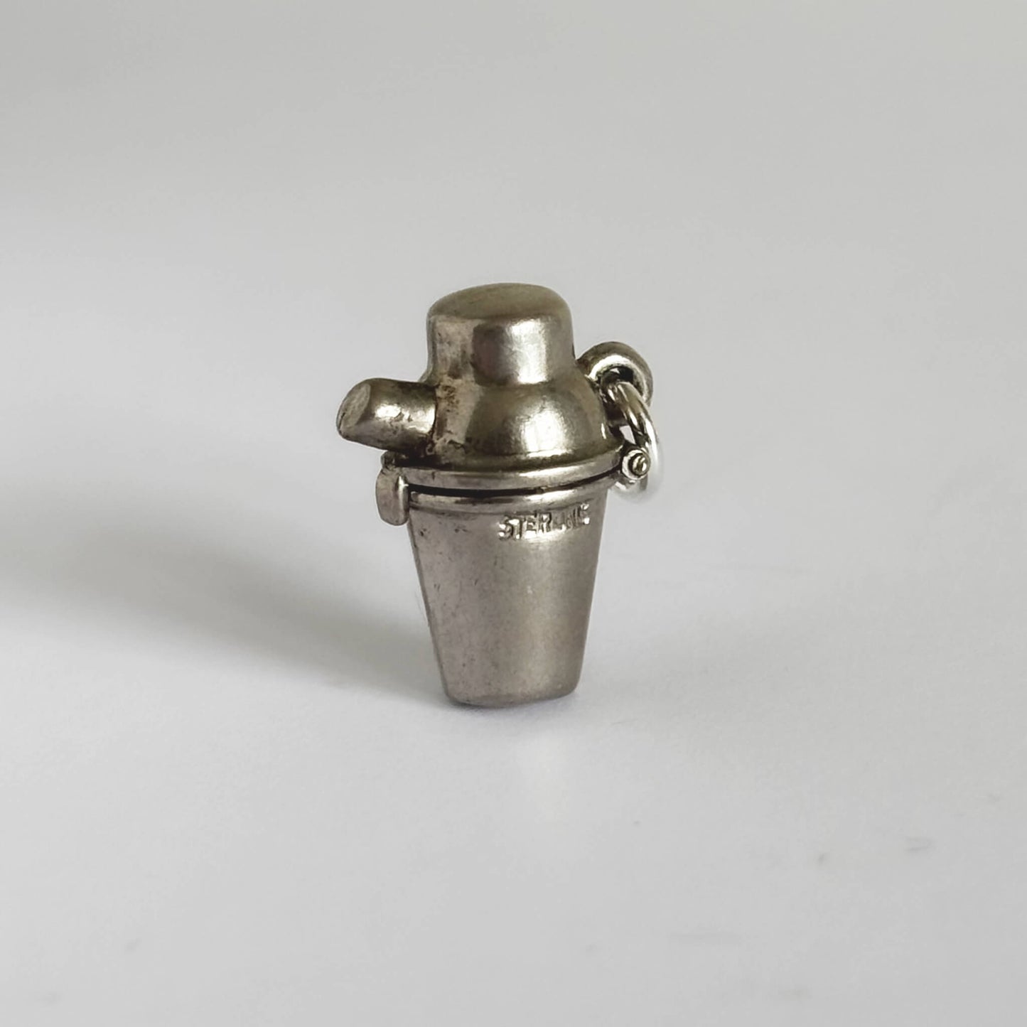 Silver cocktail shaker charm on a light gray background