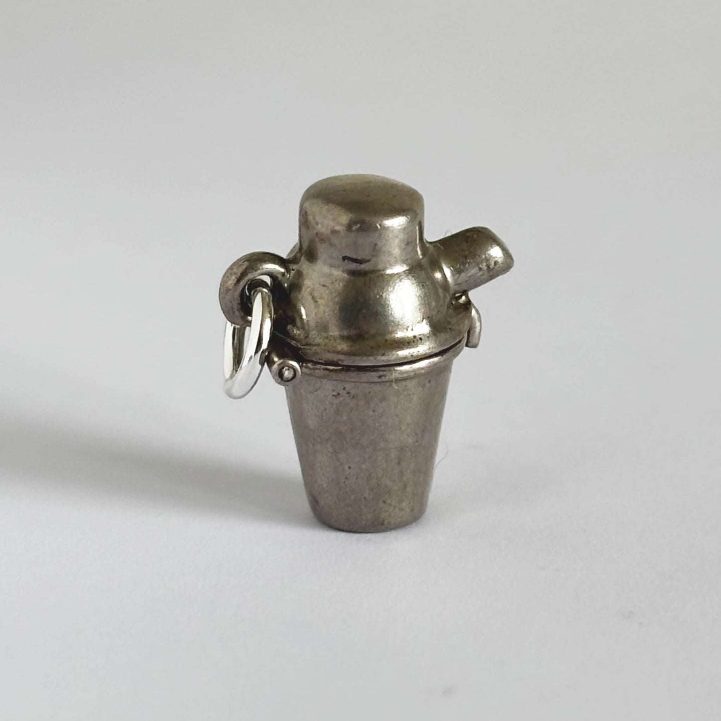 Metallic charm shaped like a cocktail shaker on a plain background