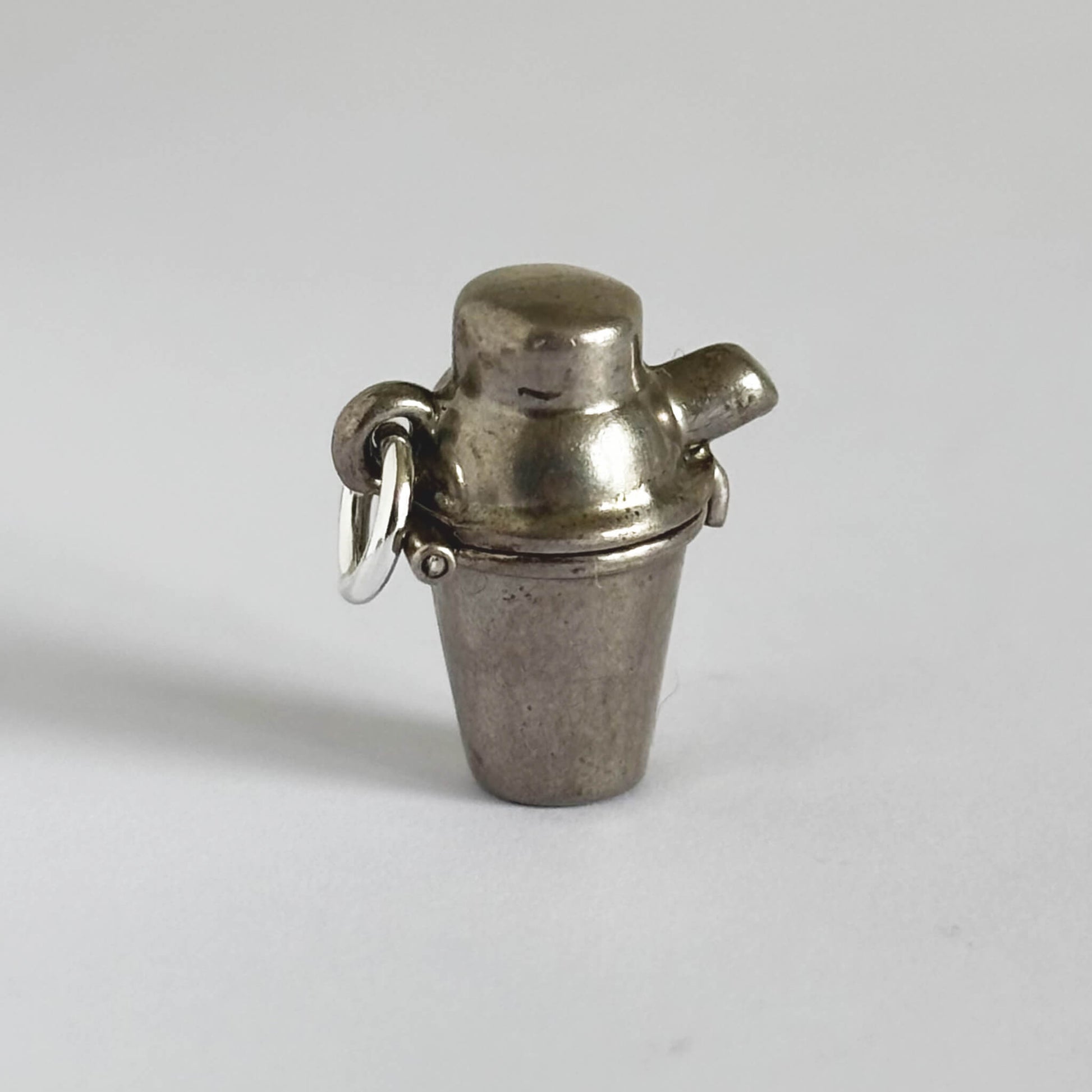 Metallic charm shaped like a cocktail shaker on a plain background