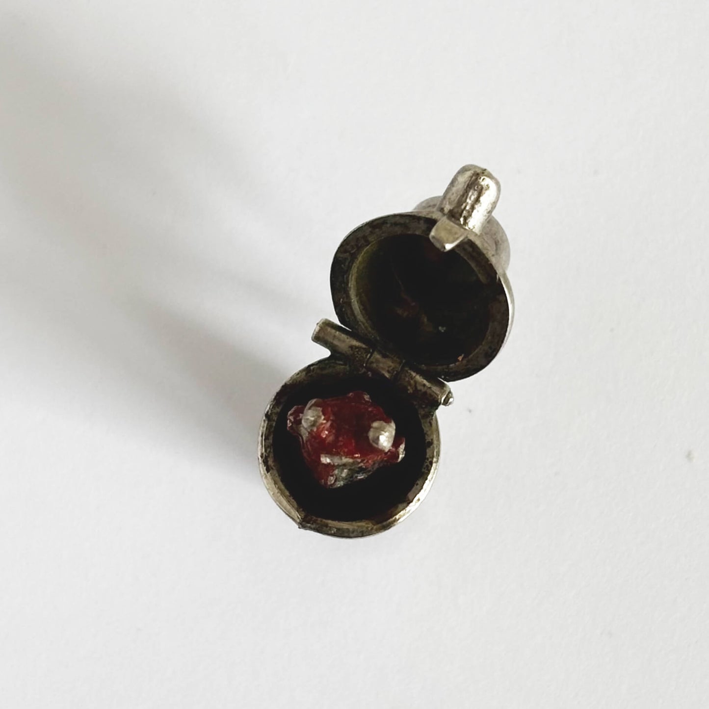 Vintage silver cocktail shaker charm seen from above, open to a red enamel devil on a white background