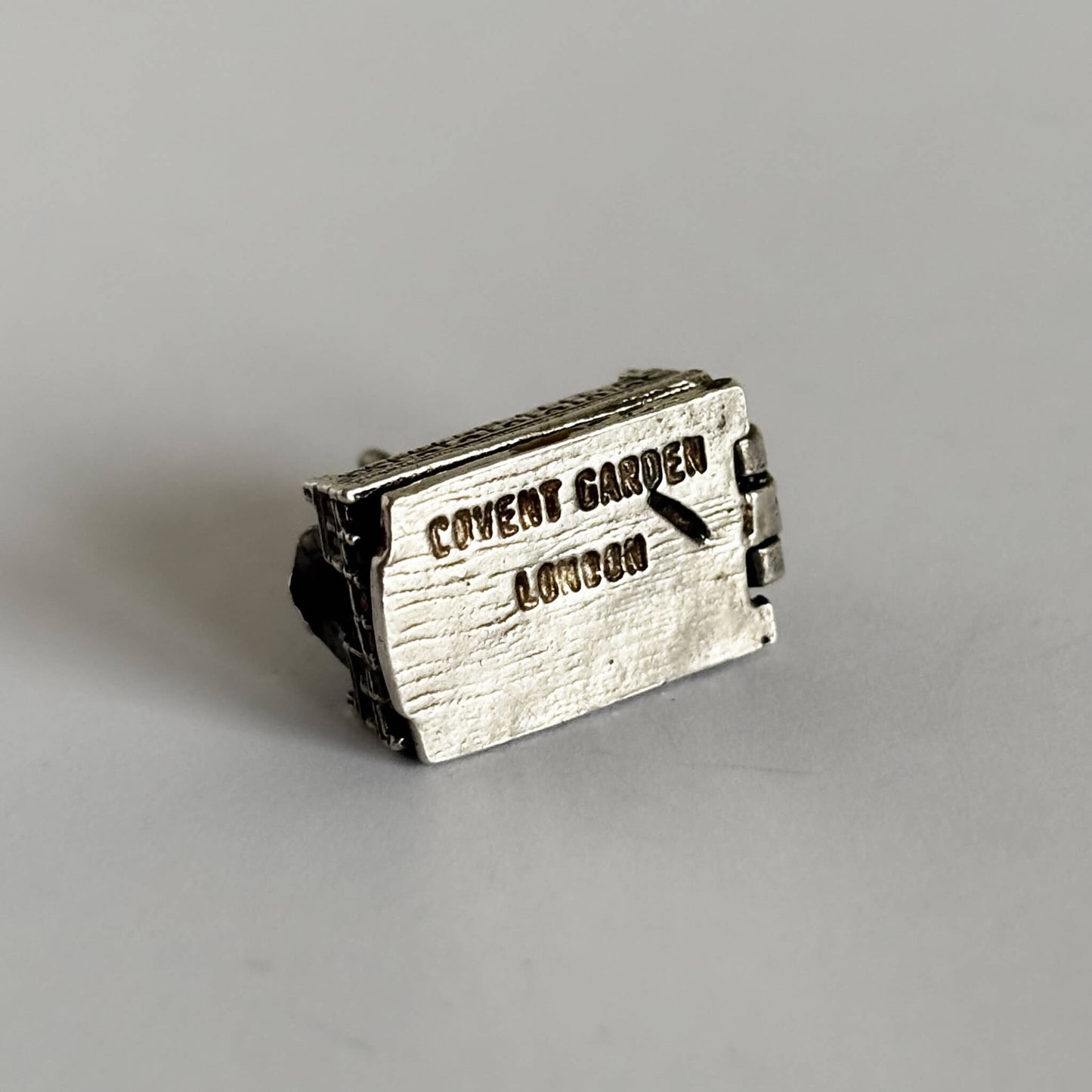 Bottom of a silver Covent Garden charm showing words COVENT GARDEN LONDON on a white background
