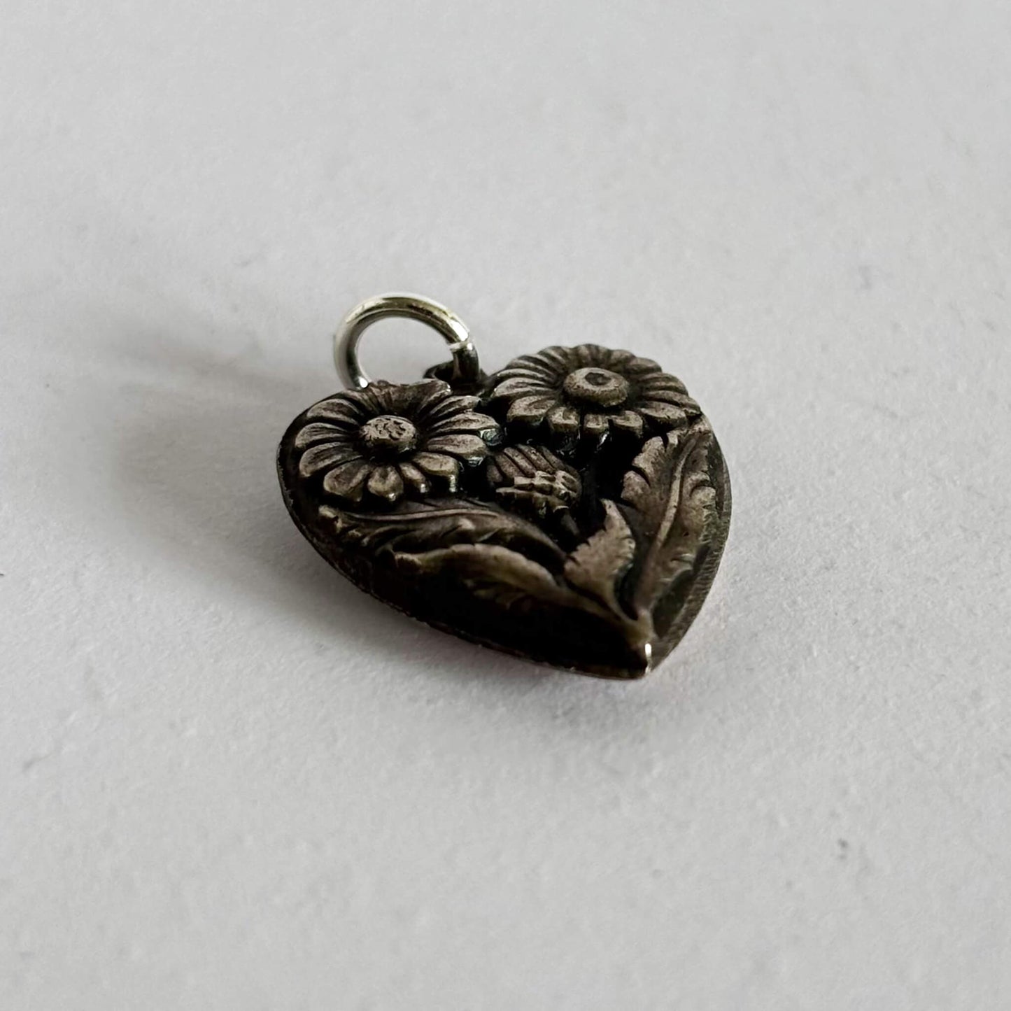 Silver heart-shaped pendant with floral designs on a light gray background